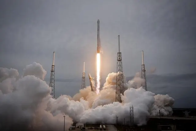 A commercial rocket lifting off from a launch pad surrounded by steam and smoke
