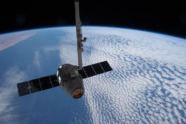 A Dragon cargo spacecraft held by the ISS robotic arm above Earth