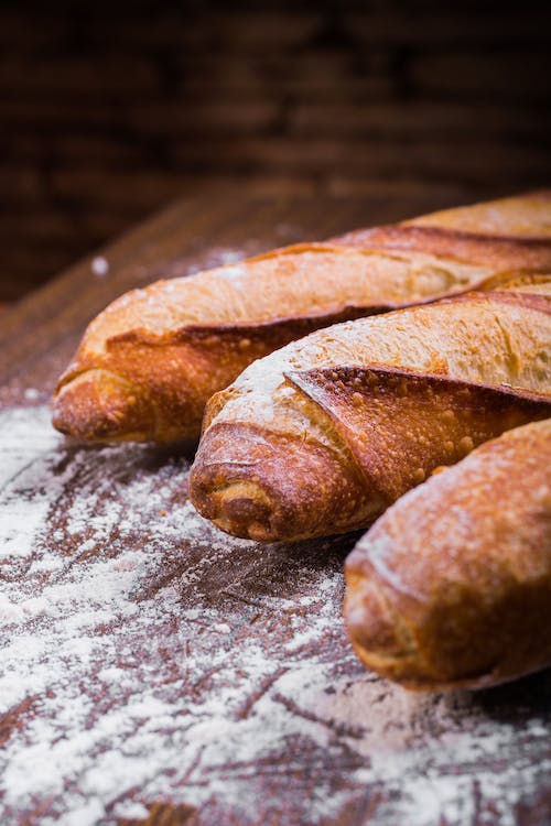 Free Close-up Photo of Three Baguettes on Brown Wooden Surface With White Powder Stock Photo