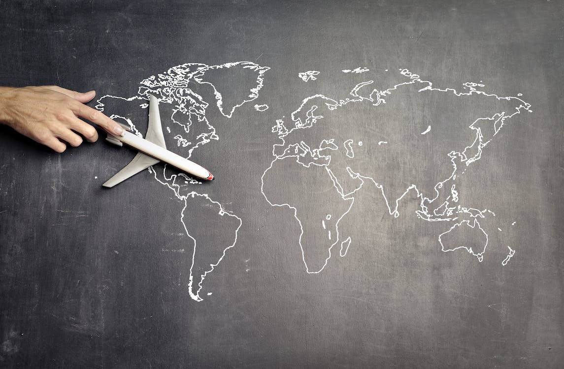 Free From above of crop anonymous person driving toy airplane on empty world map drawn on blackboard representing travel concept Stock Photo