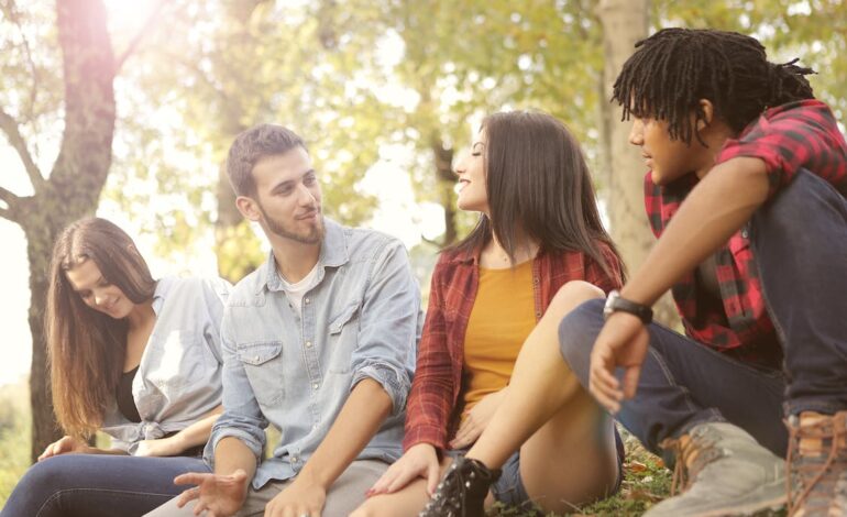 Free From below of diverse young people in casual clothes sitting on grass and talking Stock Photo