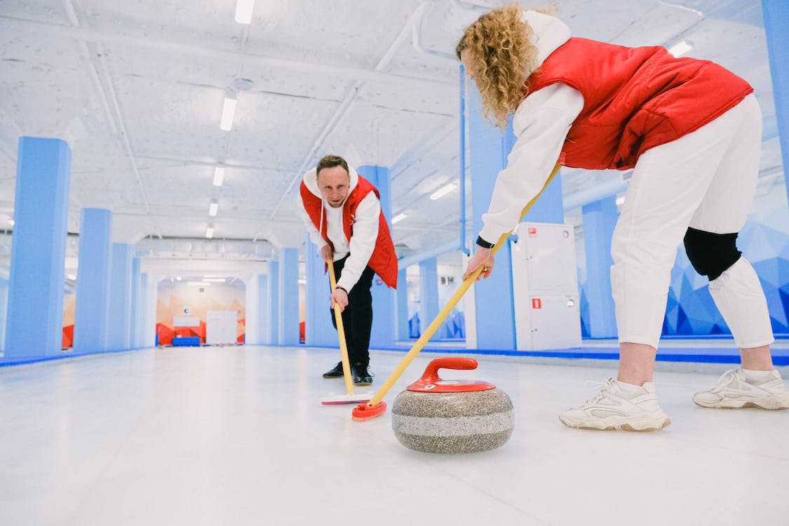 Free Low angle of male and female players sweeping ice sheet with brooms in path of granite stone during curling training Stock Photo