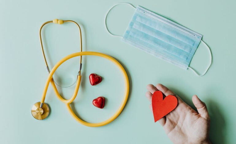 Free Top view of crop anonymous person hand with red paper heart on table with stethoscope and medical mask for coronavirus prevention Stock Photo