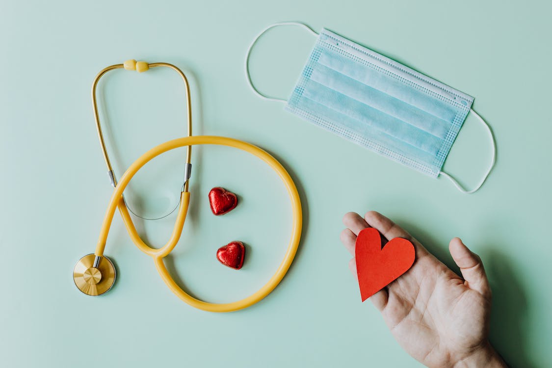 Free Top view of crop anonymous person hand with red paper heart on table with stethoscope and medical mask for coronavirus prevention Stock Photo