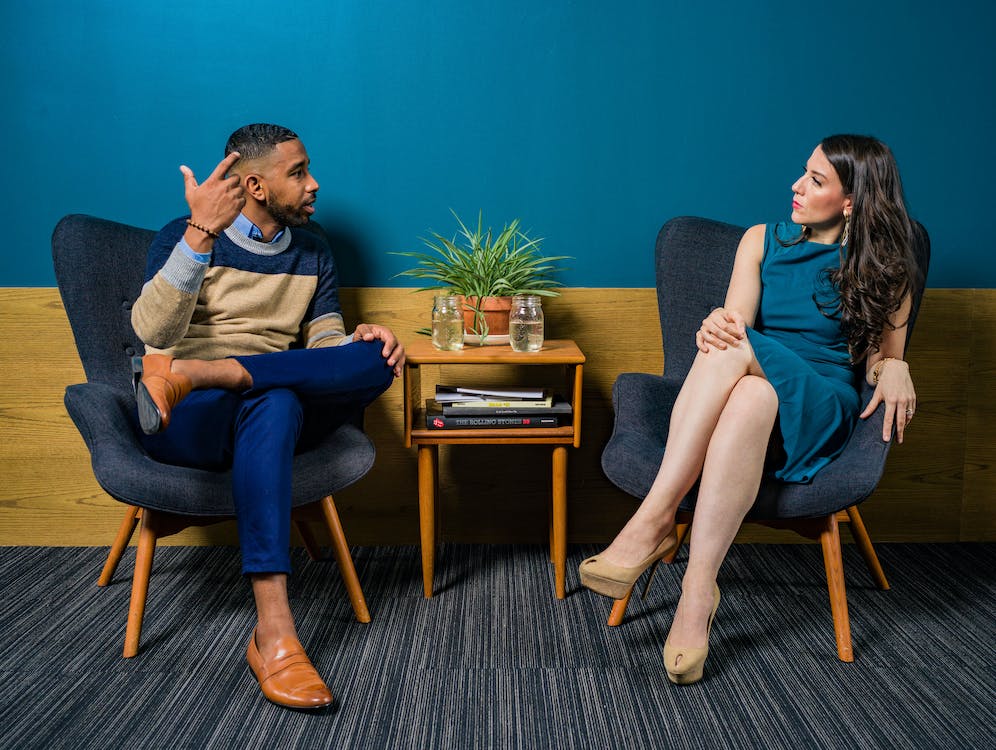 Free Woman Wearing Teal Dress Sitting on Chair Talking to Man Stock Photo