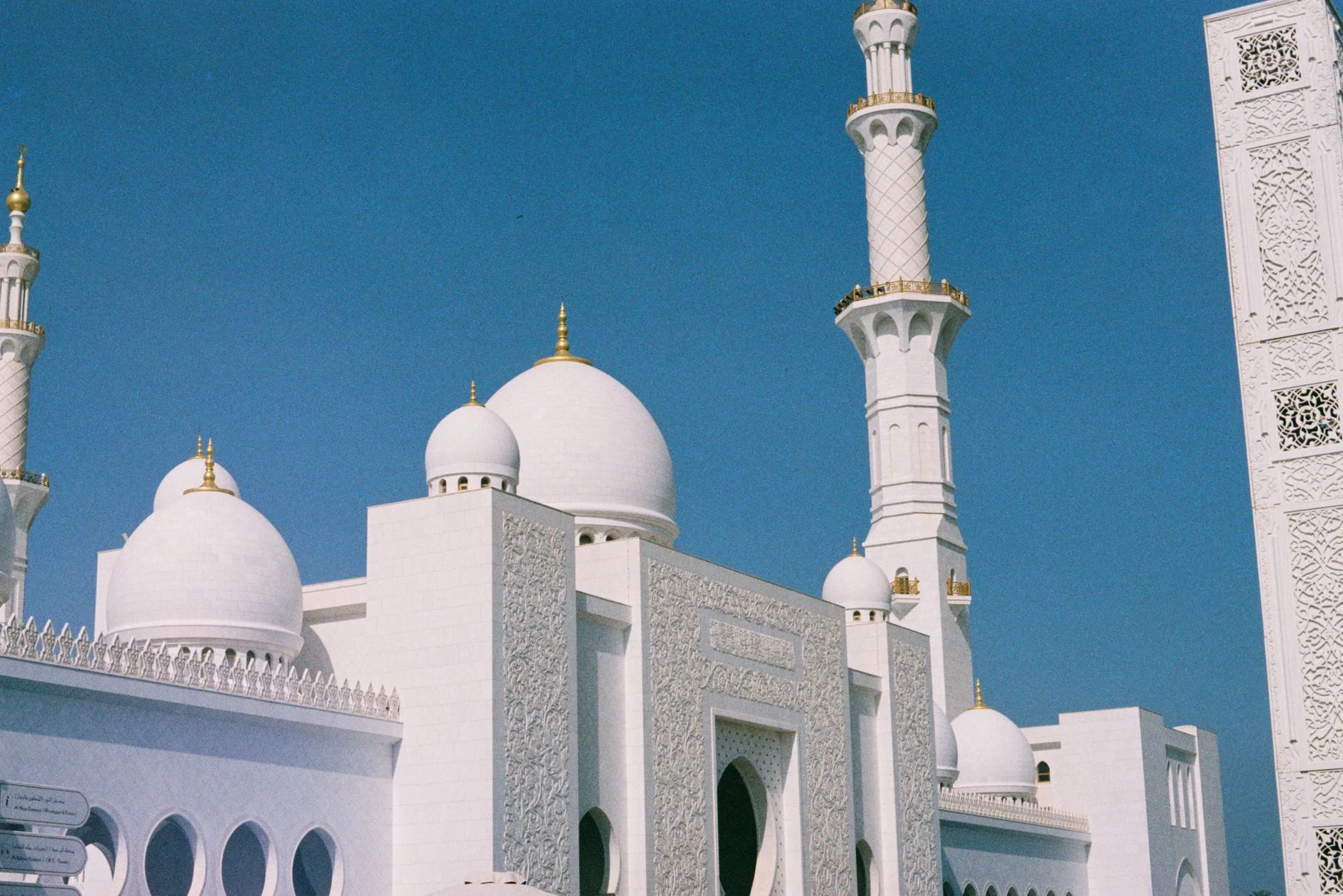 White domes and minarets of the Sheikh Zayed Grand Mosque in Abu Dhabi under a blue sky