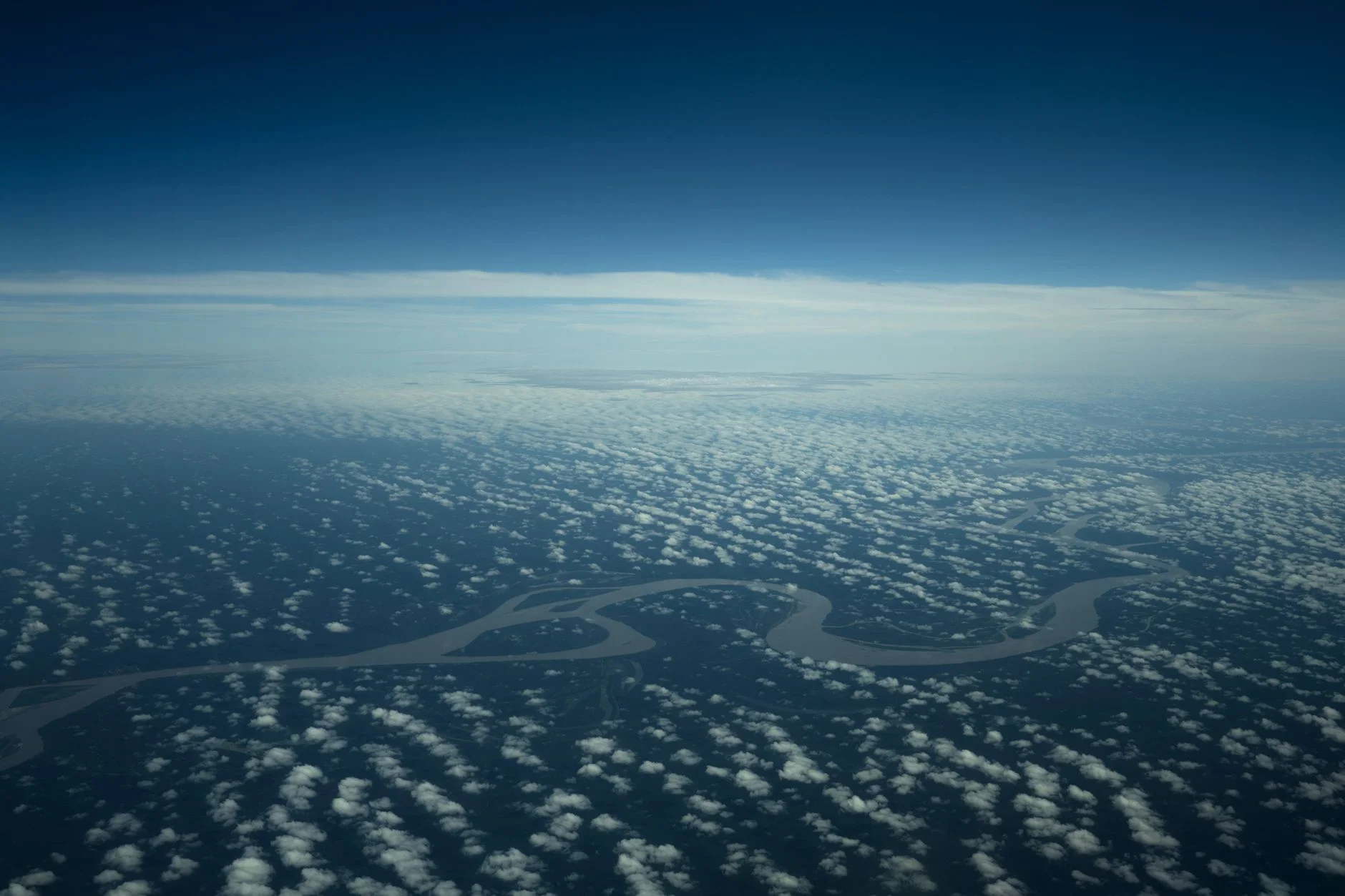 A river winding through rainforest seen from above with clouds below the horizon
