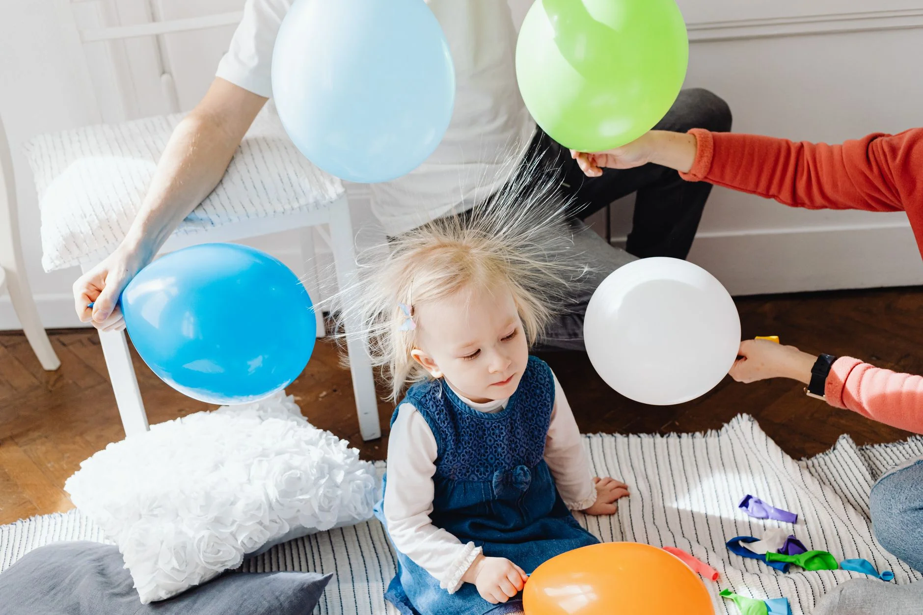 A toddler sitting among balloons with fine hair standing up from static electricity