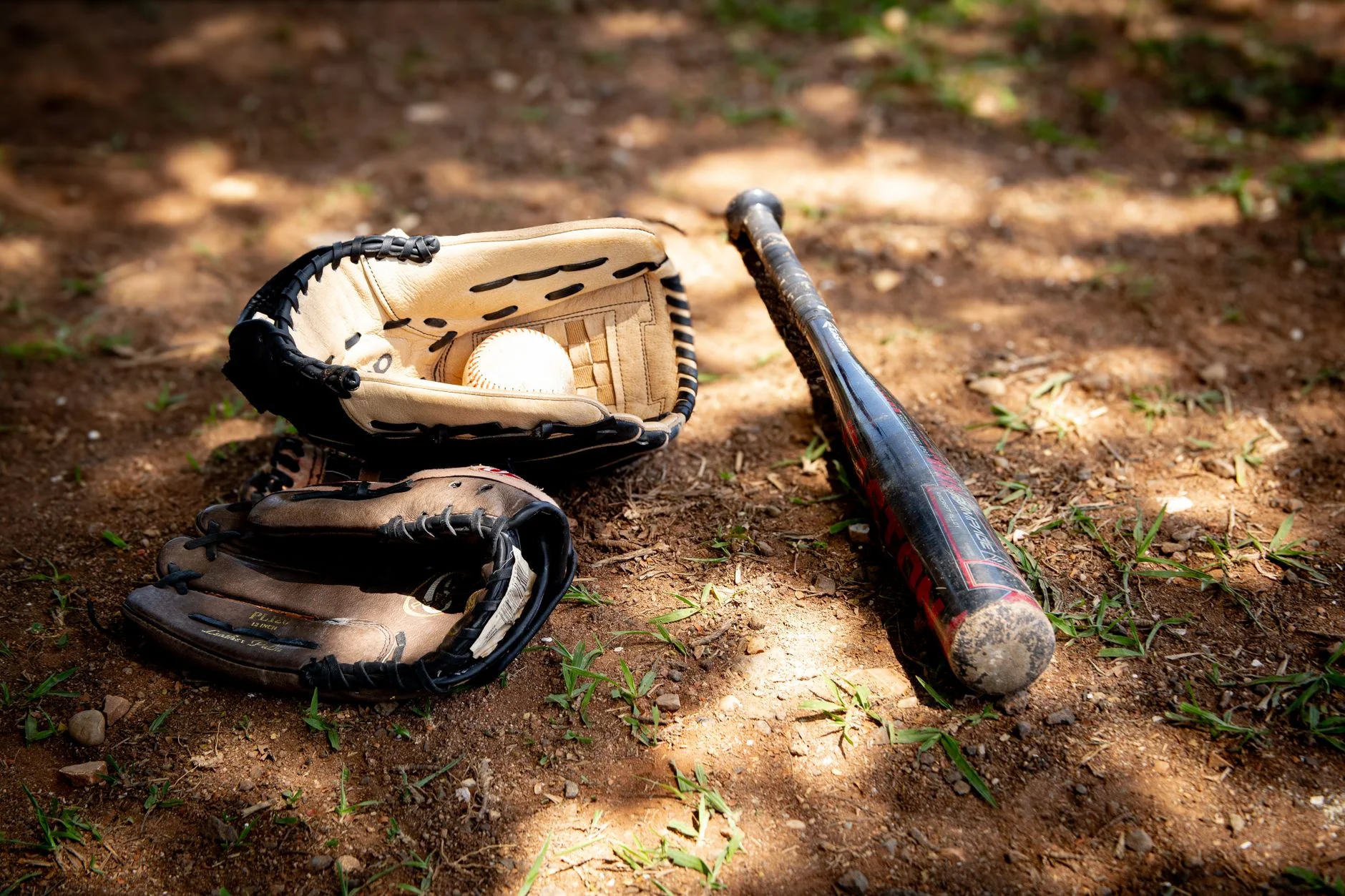 Baseball bat and gloves lying on a dusty field
