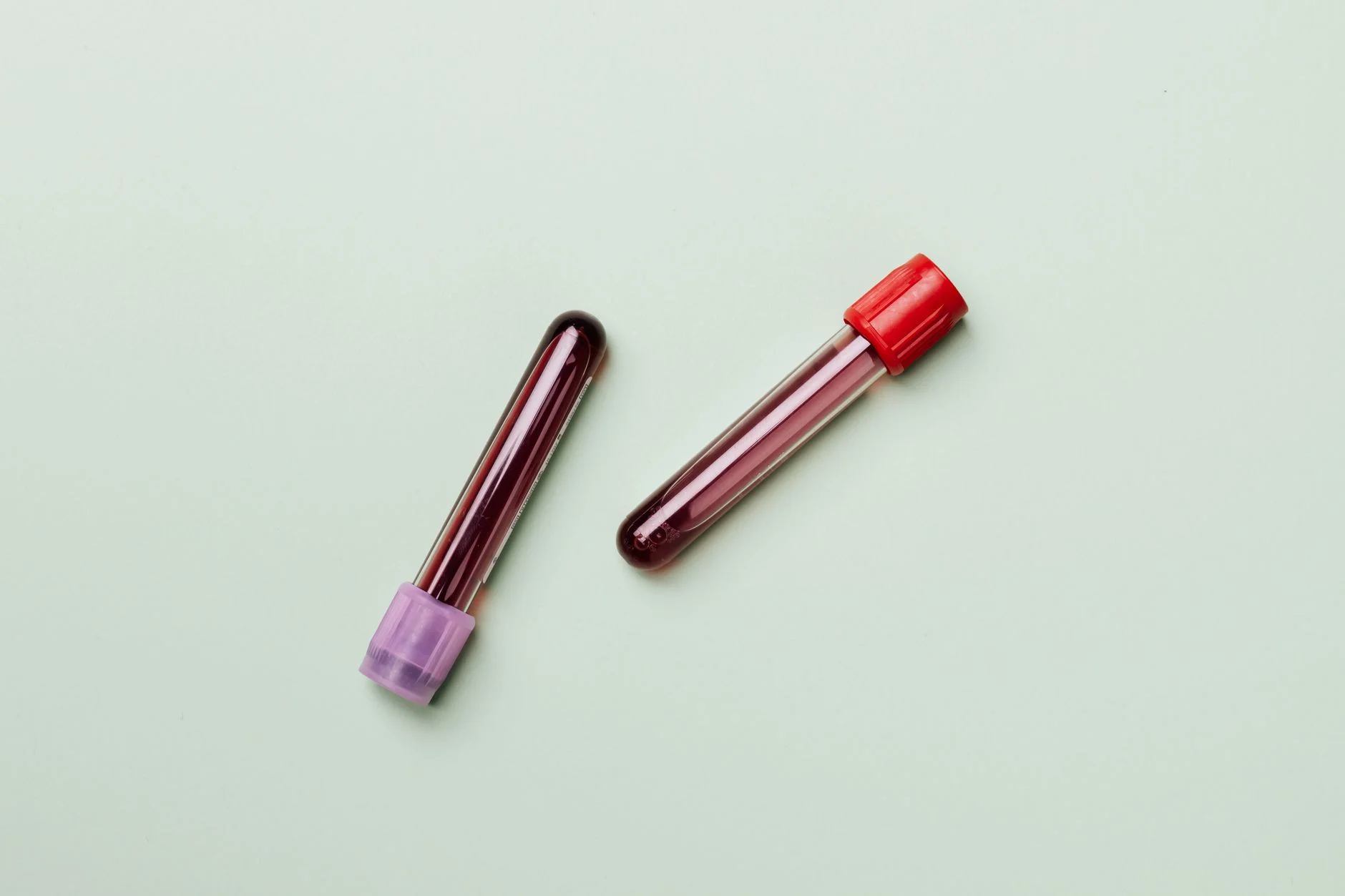 Two blood sample tubes with purple and red caps lying on a pale green surface