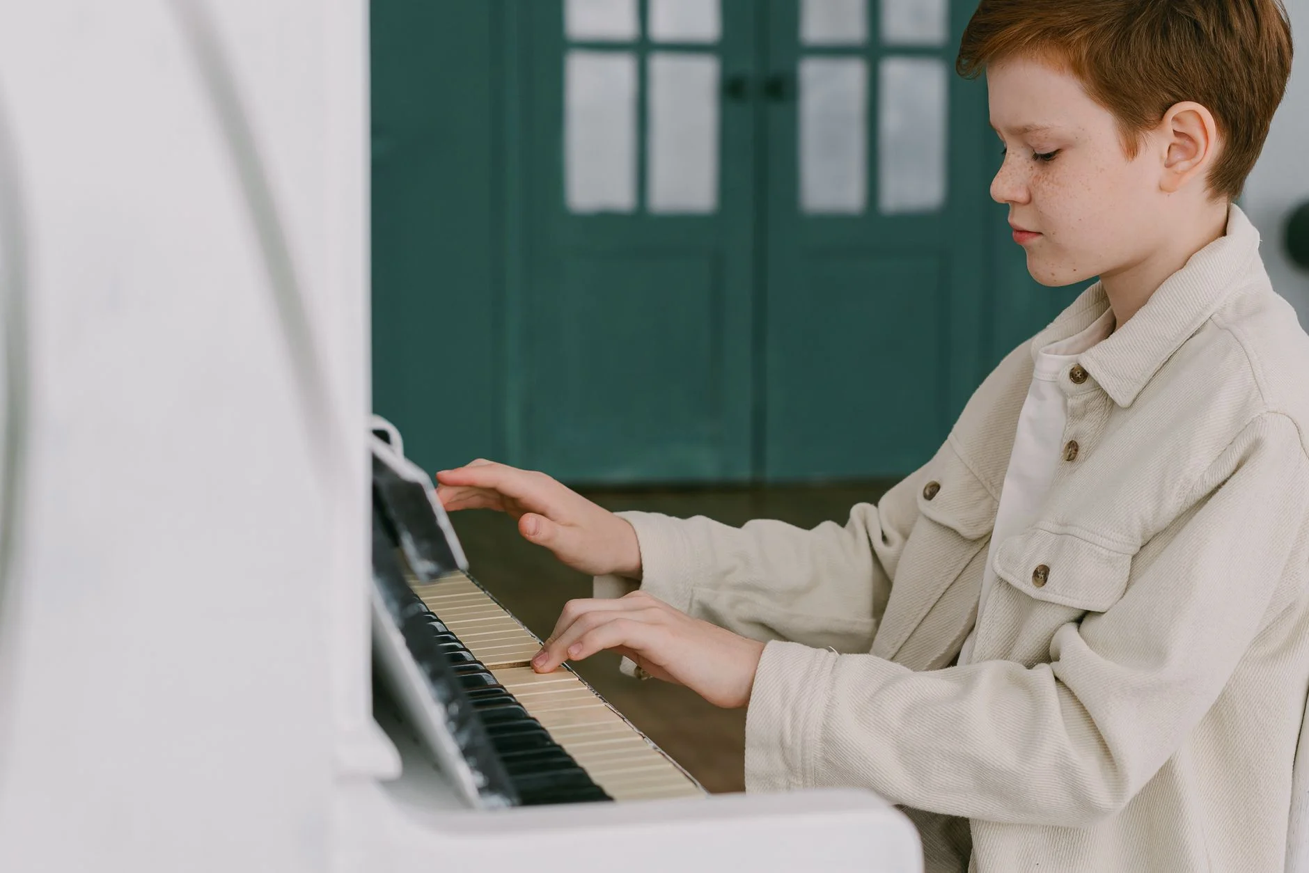 A boy in a cream jacket playing an upright piano