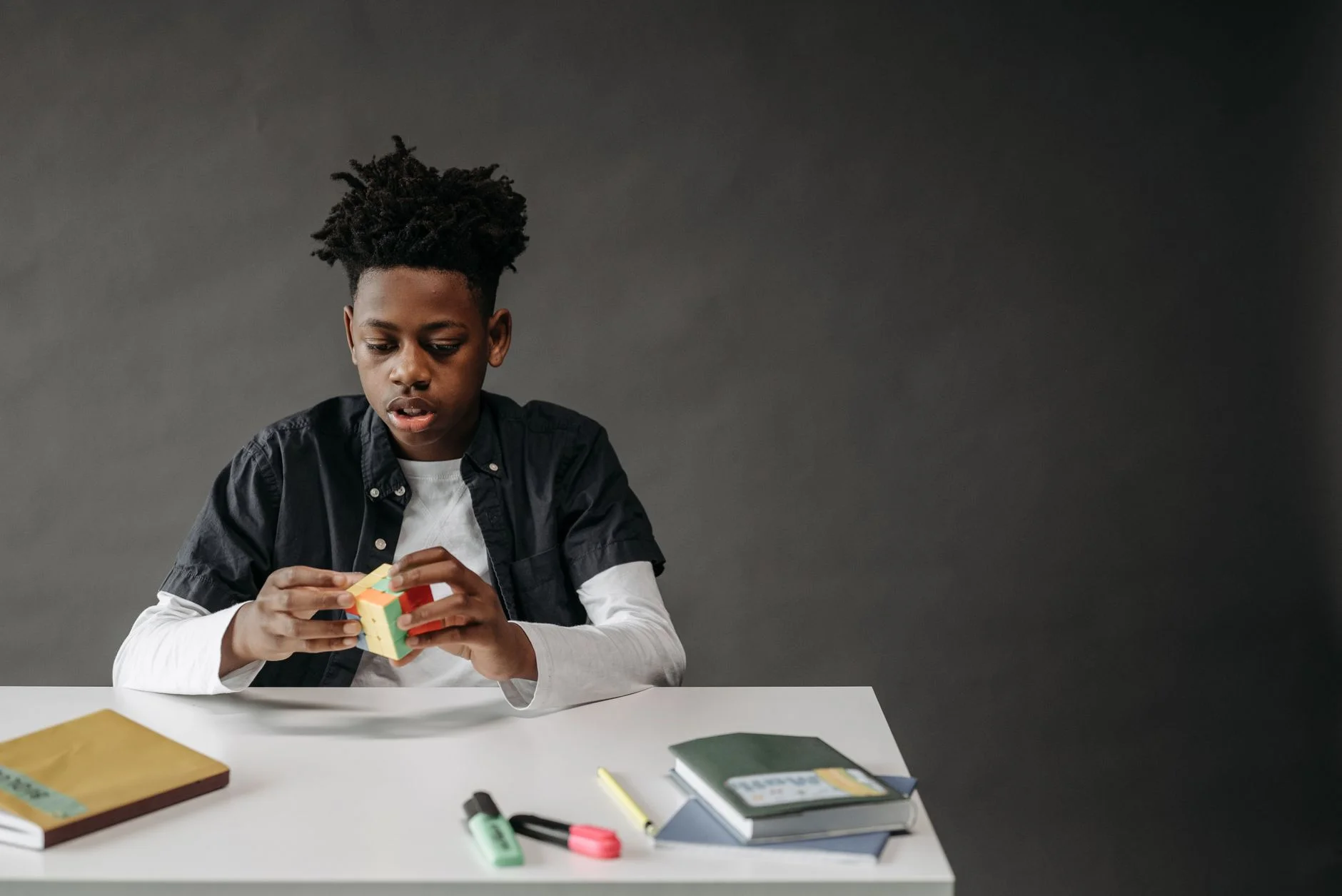 A boy at a desk concentrating on solving a small puzzle cube