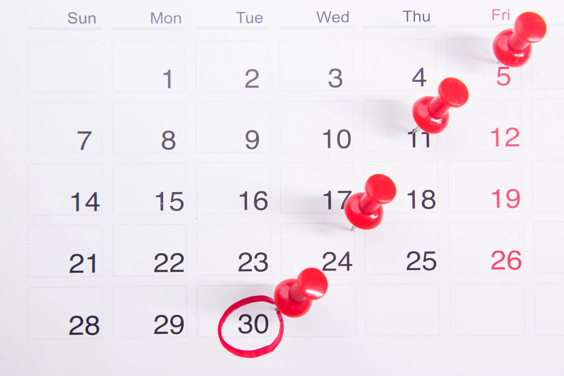 A paper calendar with red push pins marking dates and the 30th circled in red pen