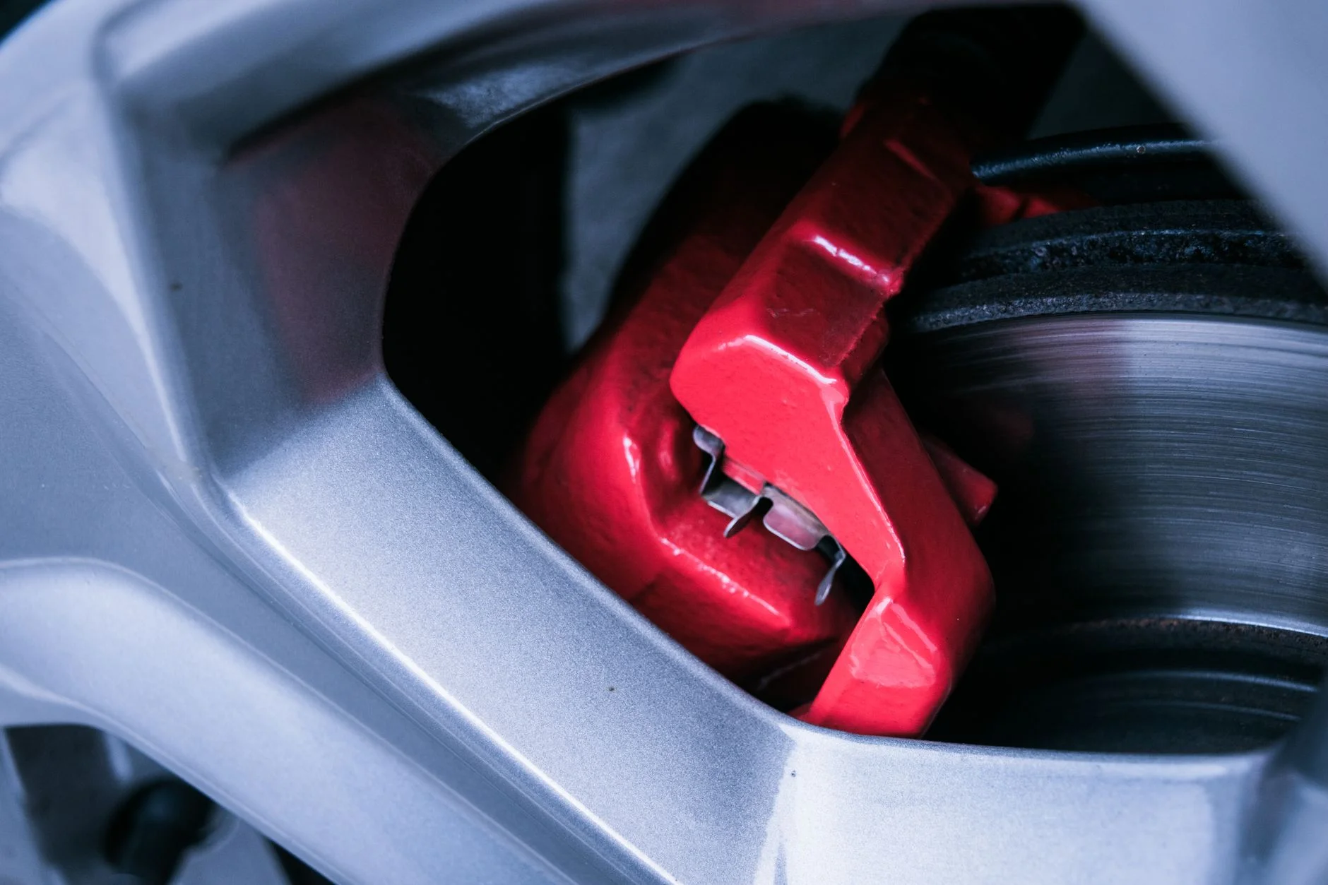 Close-up of a red brake caliper gripping a car’s brake disc behind an alloy wheel