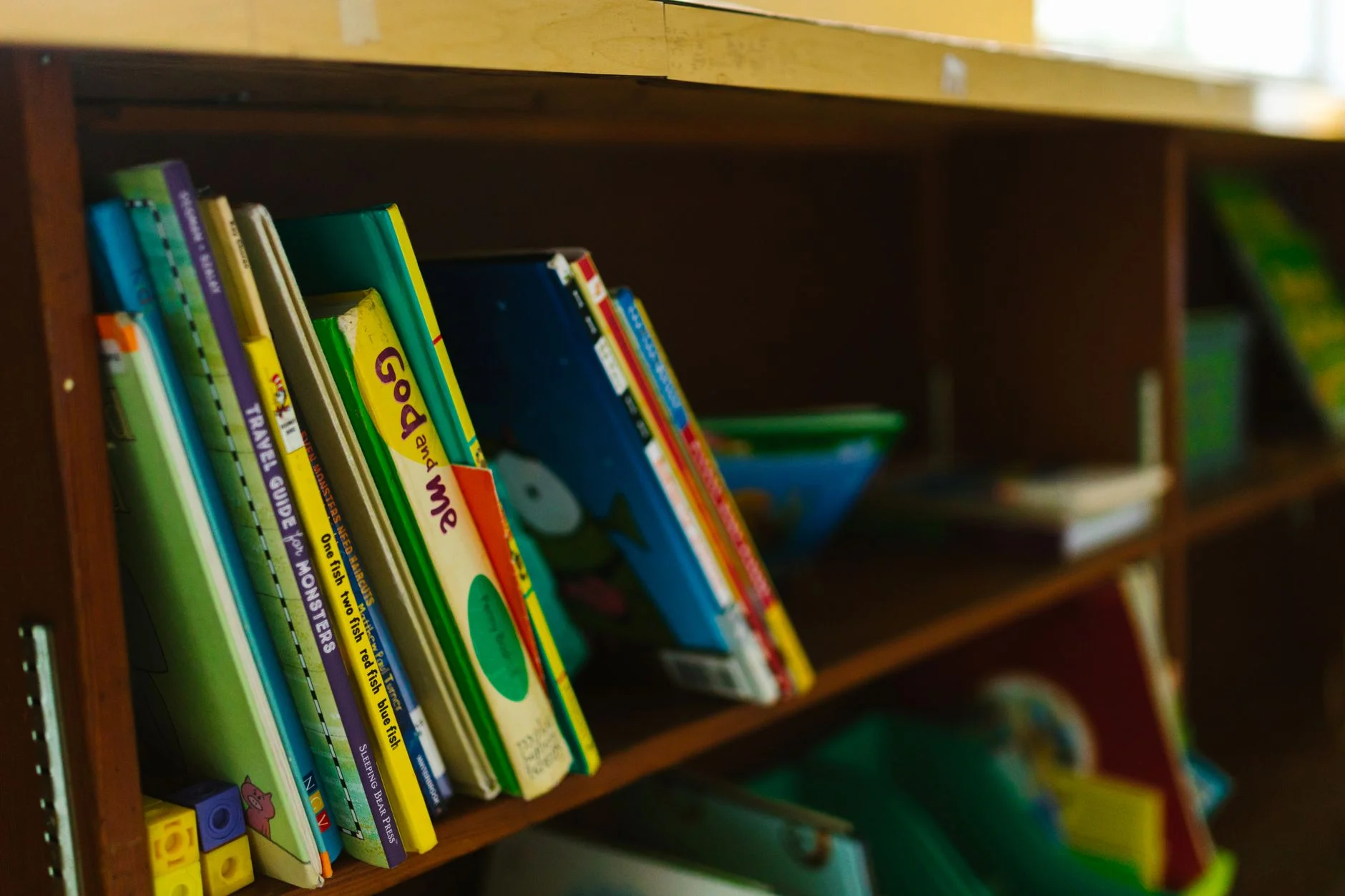 Colourful children’s books standing on a brown wooden shelf