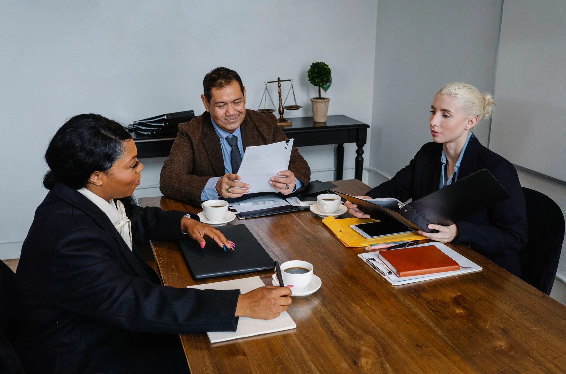 Three colleagues in formal clothes discussing documents around a wooden meeting table