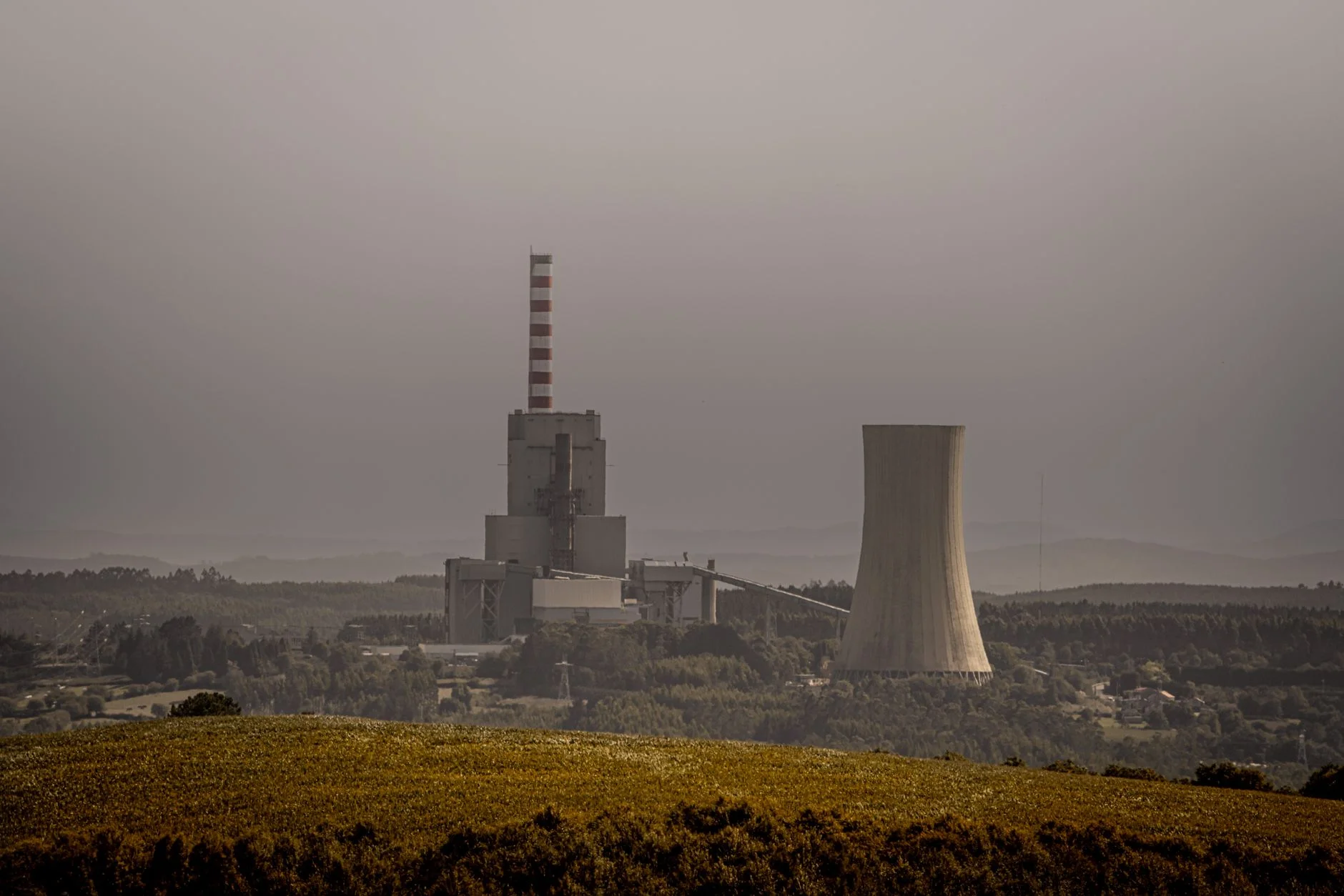 A coal-fired power station with a tall chimney and a cooling tower under a hazy sky