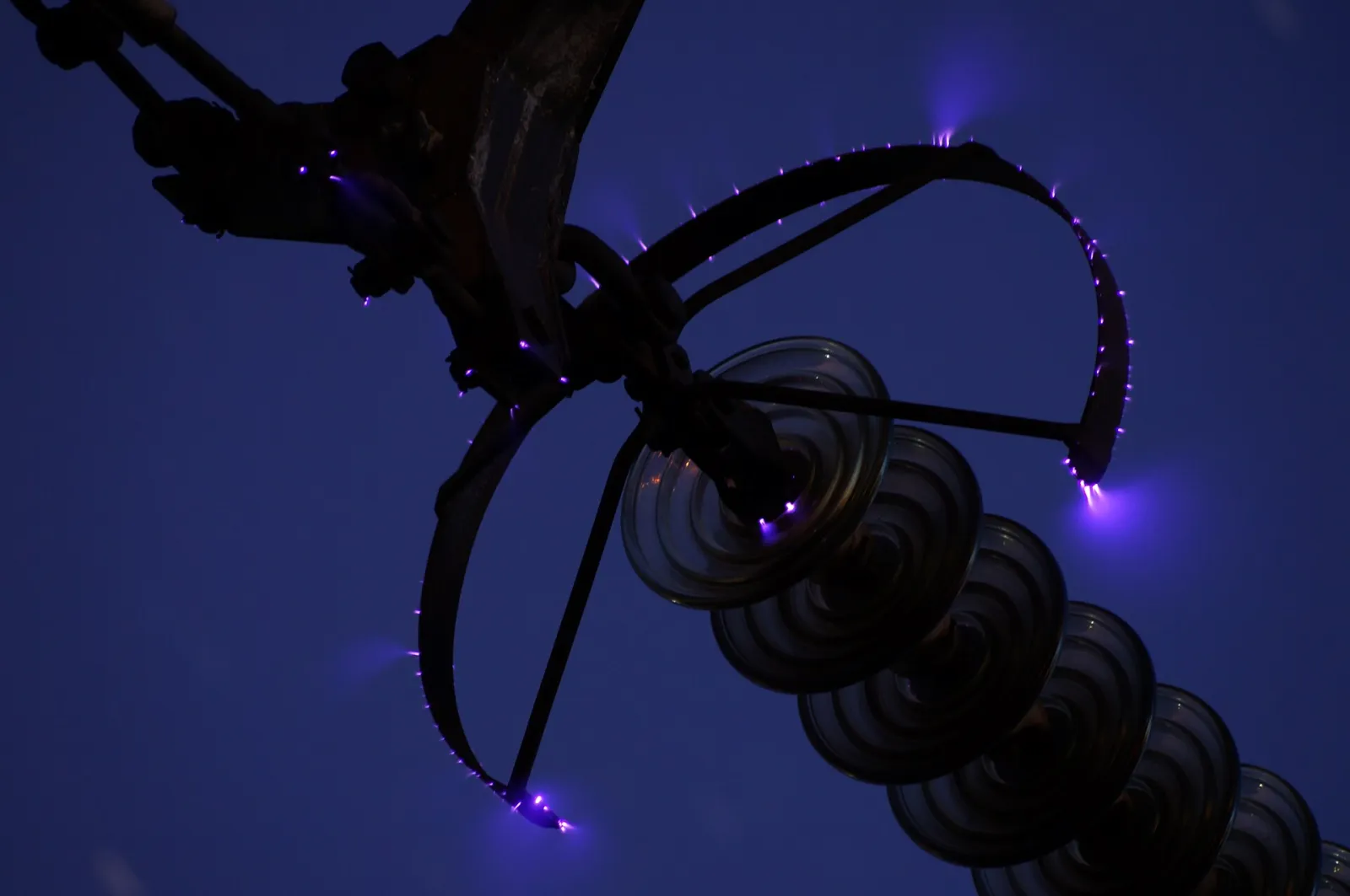 Night photo of violet corona discharge points on the corona ring and insulator string of a 500 kV power line