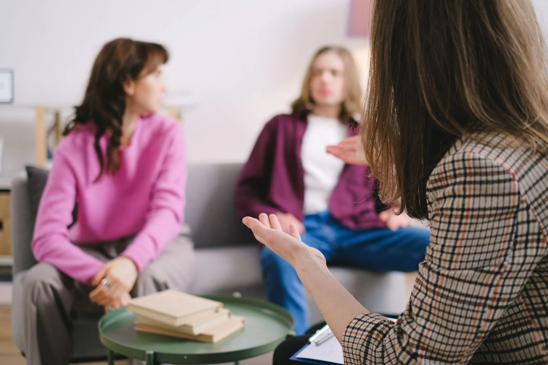 Two people on a sofa talking with a counsellor holding a clipboard