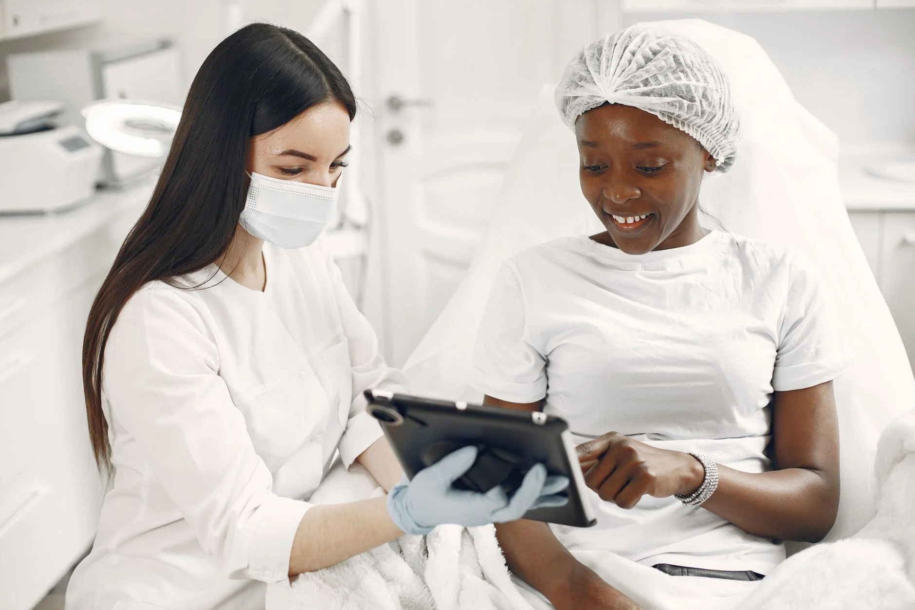 A practitioner in a mask showing a tablet to a smiling client in a clinic before a treatment