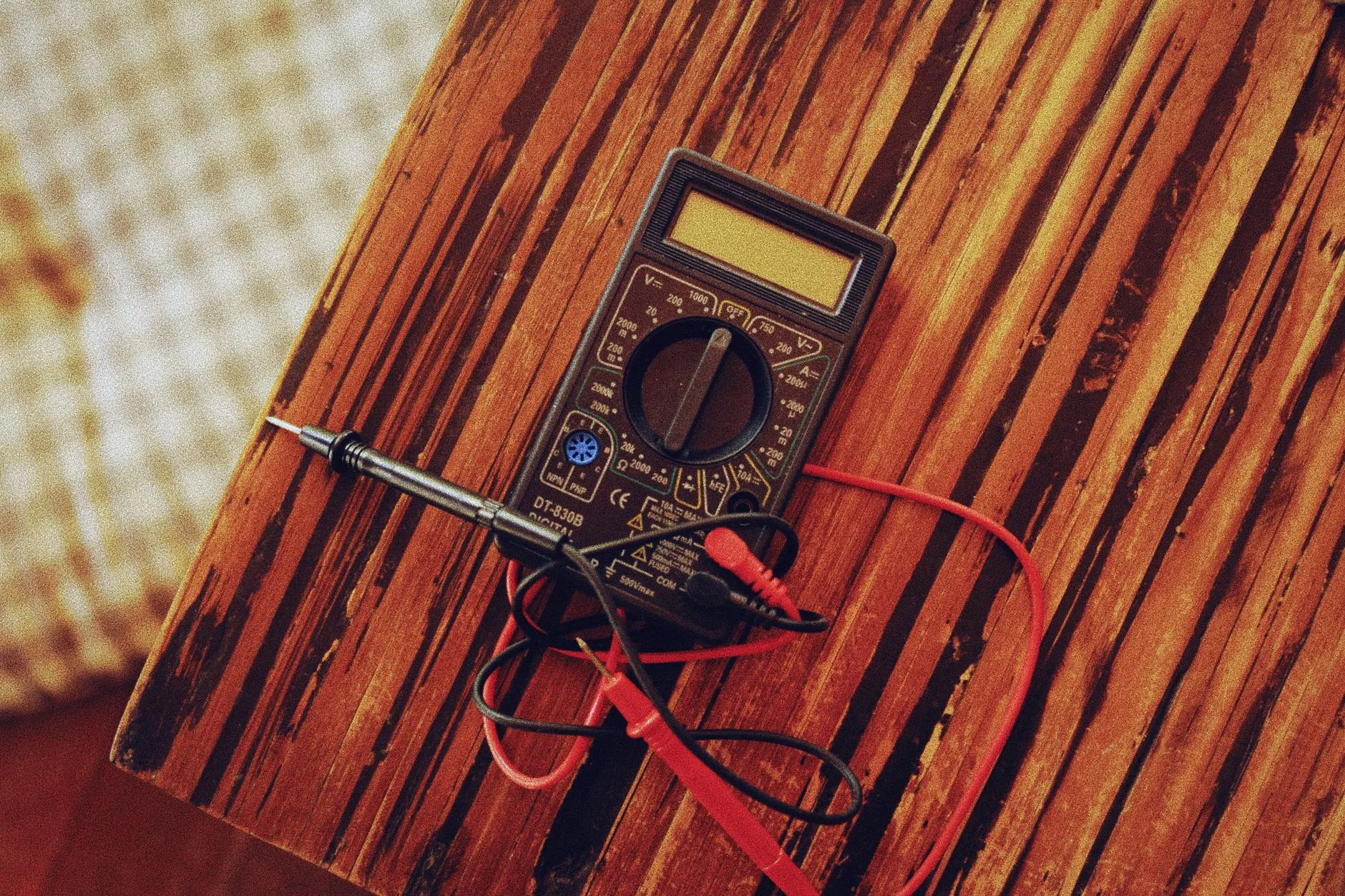 A digital multimeter with a rotary dial and red and black test leads lying on a wooden table
