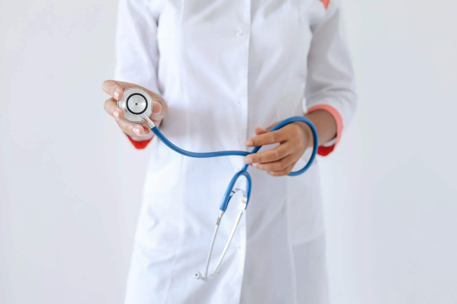 A healthcare professional in a white coat holding a blue stethoscope