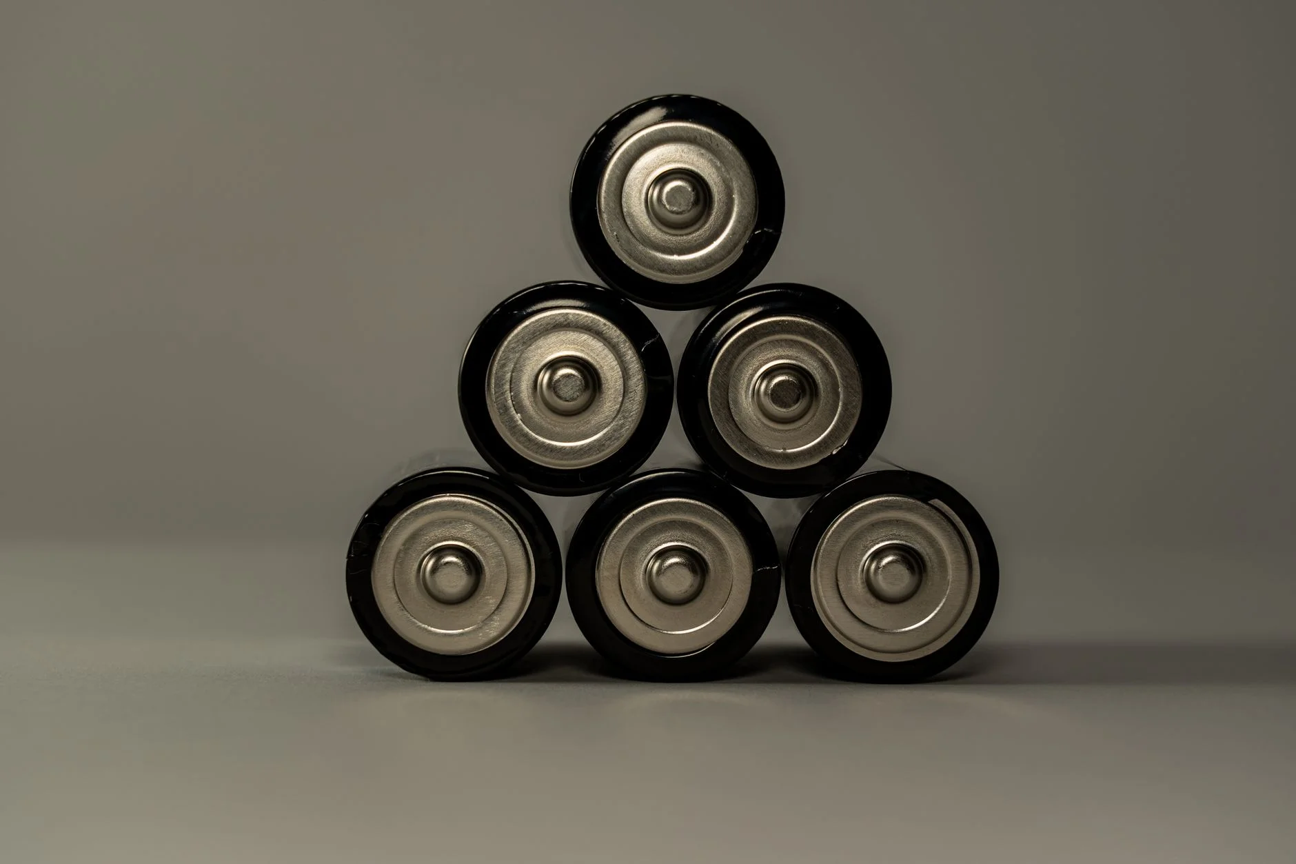 Six cylindrical AA dry cells stacked in a pyramid, showing their metal end caps, on a grey background
