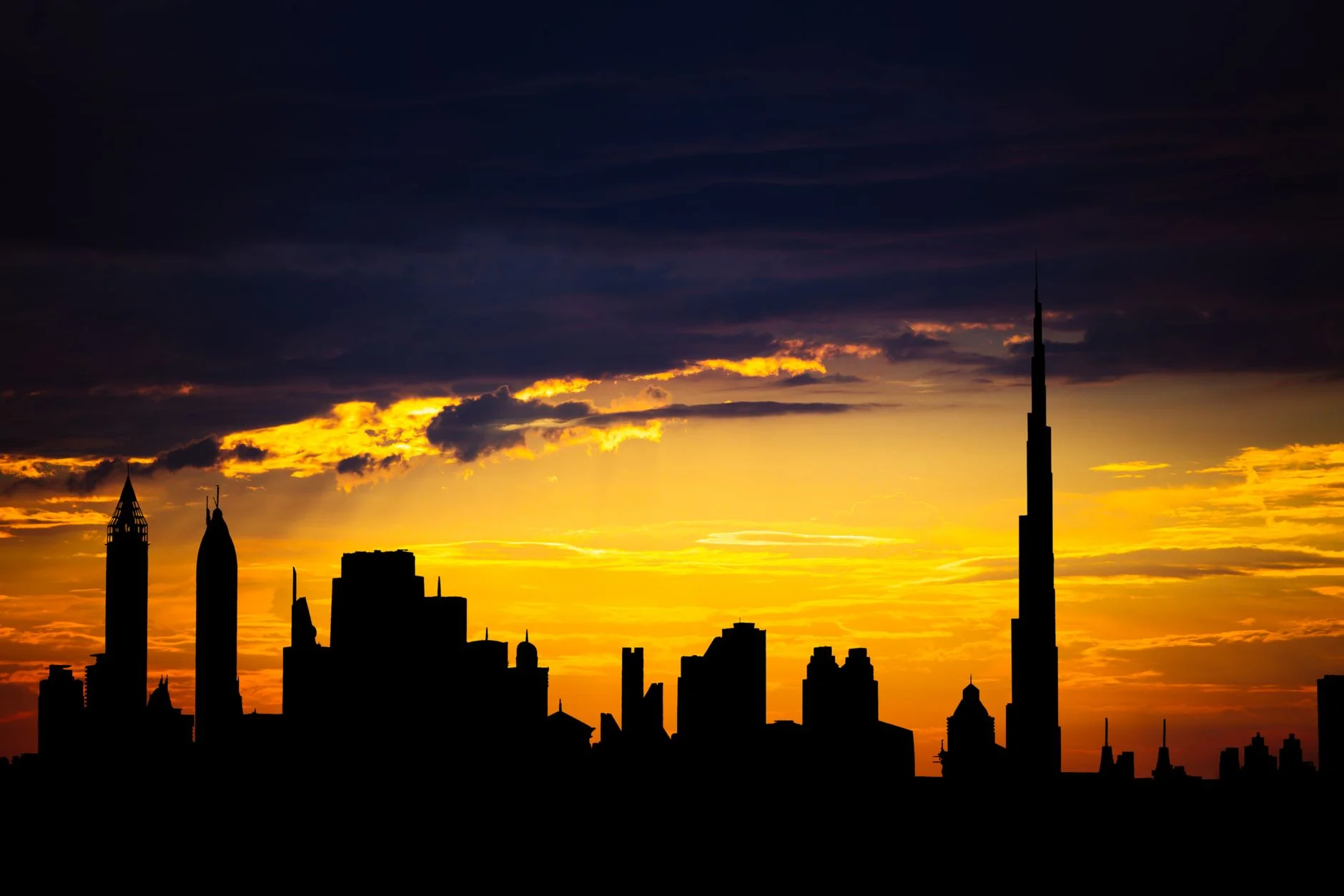 Silhouette of the Dubai skyline with the Burj Khalifa against an orange sunset