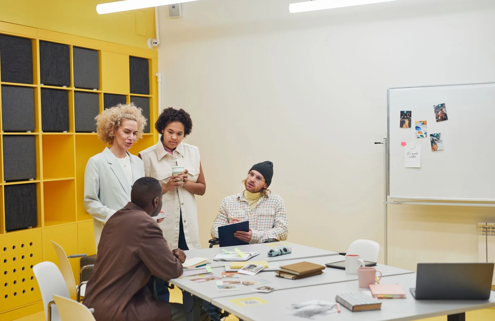 Colleagues standing and sitting around a meeting table with notebooks and a laptop, discussing a plan