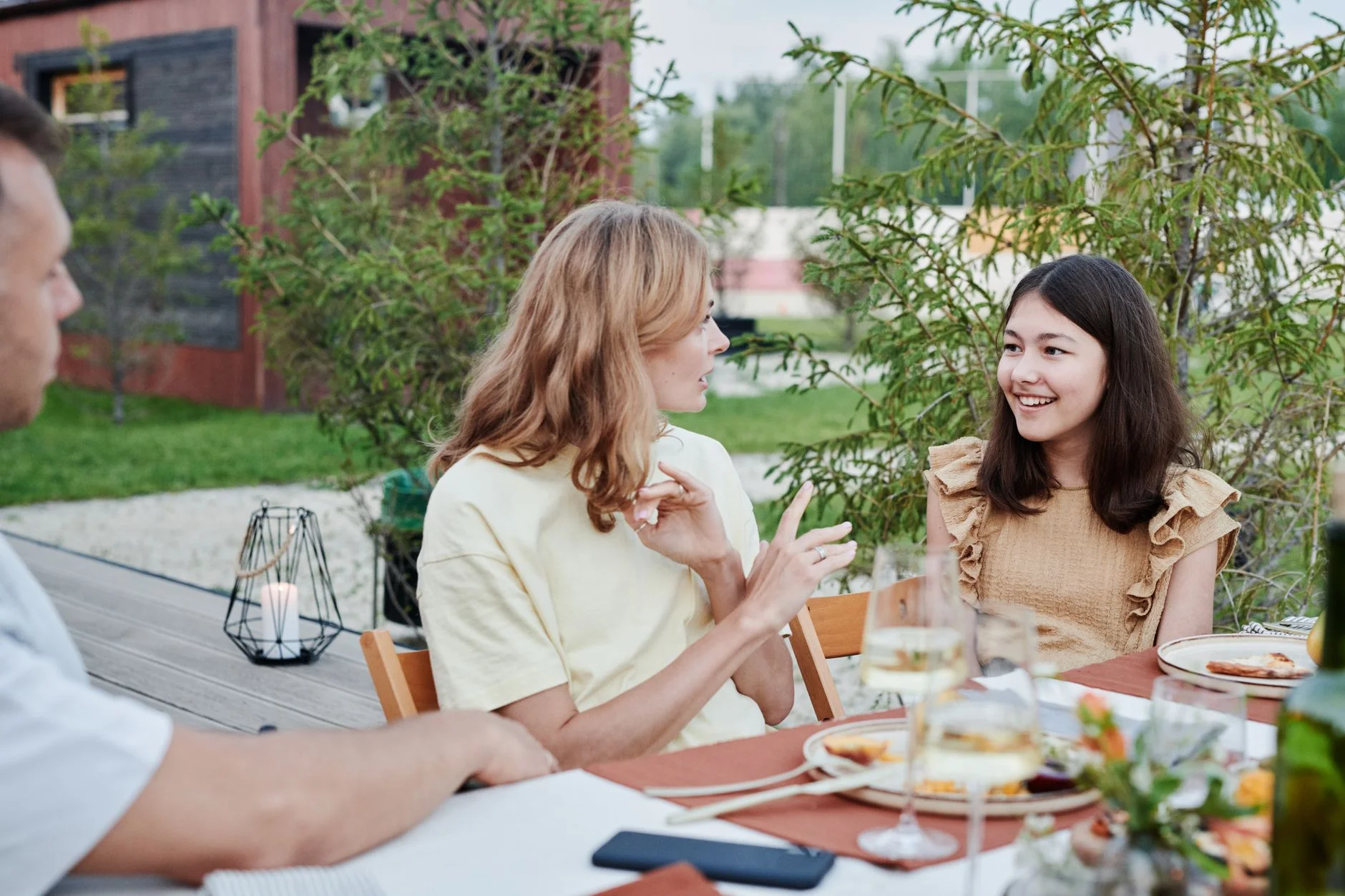 People talking and smiling around an outdoor dinner table in a garden
