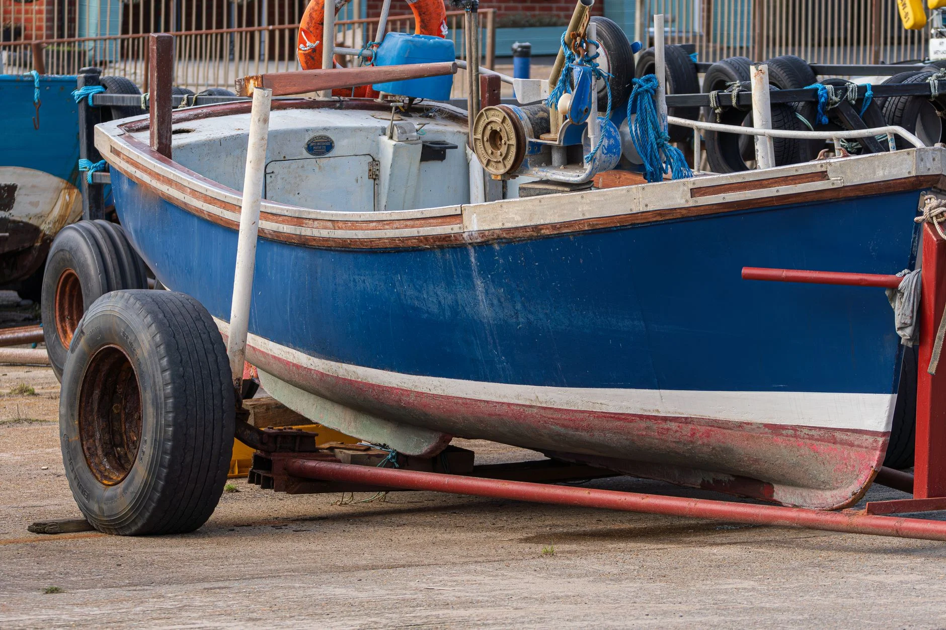 A blue and white fishing boat sitting on a wheeled trailer on a quayside