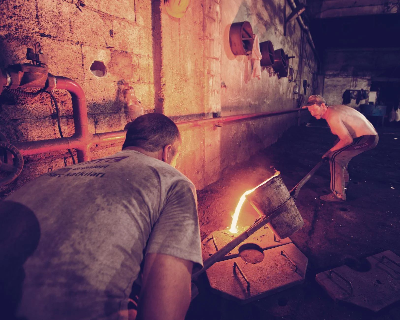 Foundry workers pouring glowing molten metal into moulds on the floor