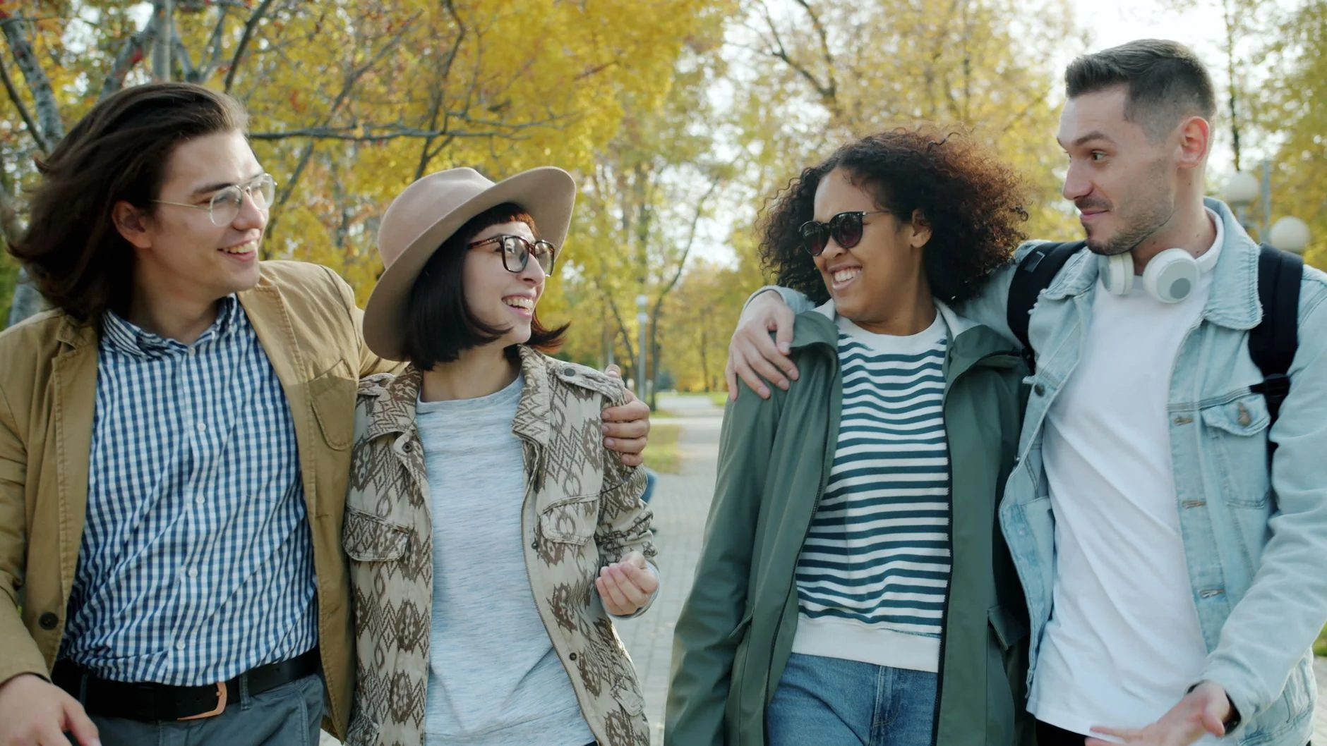 Four friends walking and chatting along a tree-lined path in an autumn park