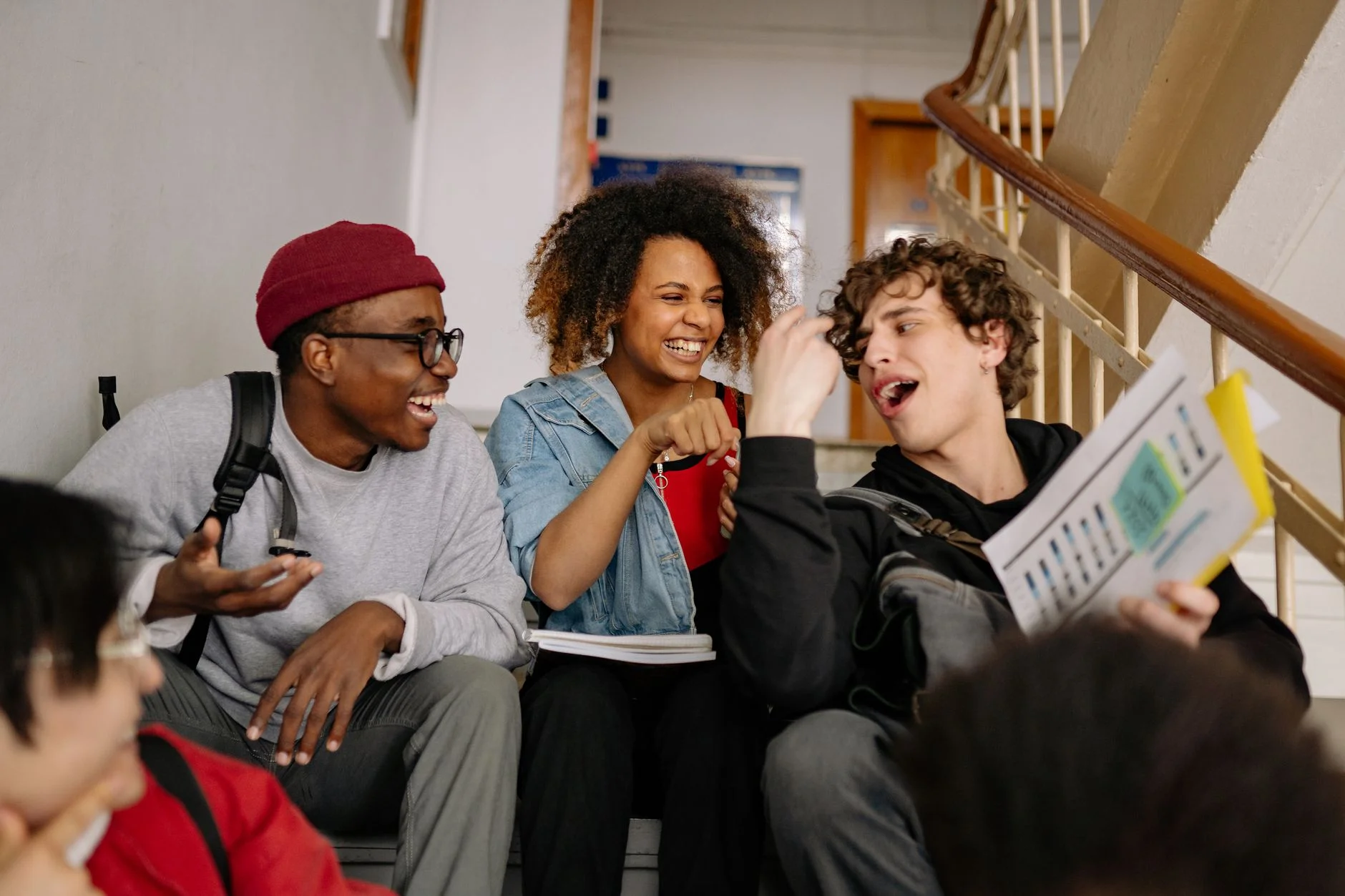 Students laughing together on a school staircase while one holds up a printed sheet