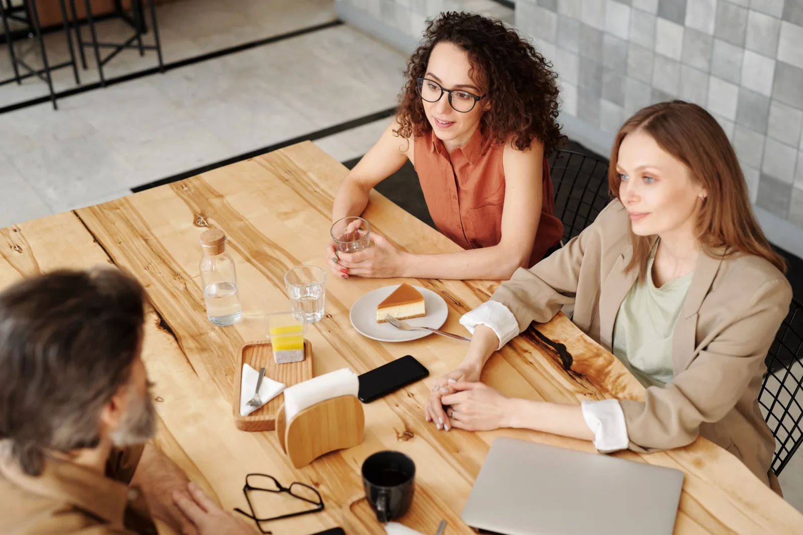 Three adults chatting around a wooden café table with coffee, cake and a laptop