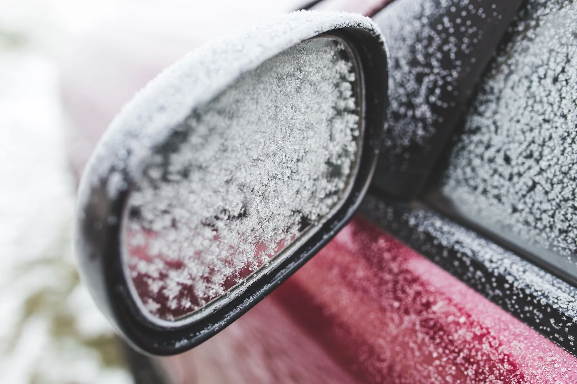 Frost crystals covering a red car’s wing mirror and side window on a cold morning