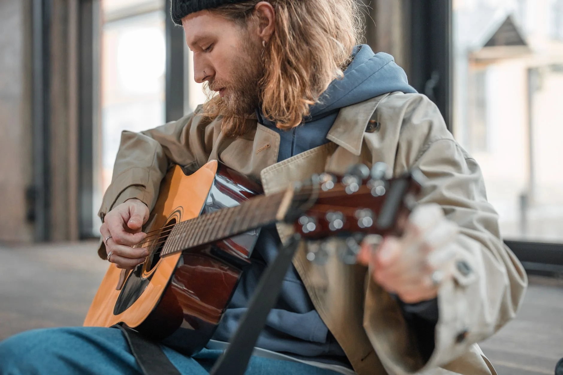 A bearded man concentrating while playing an acoustic guitar