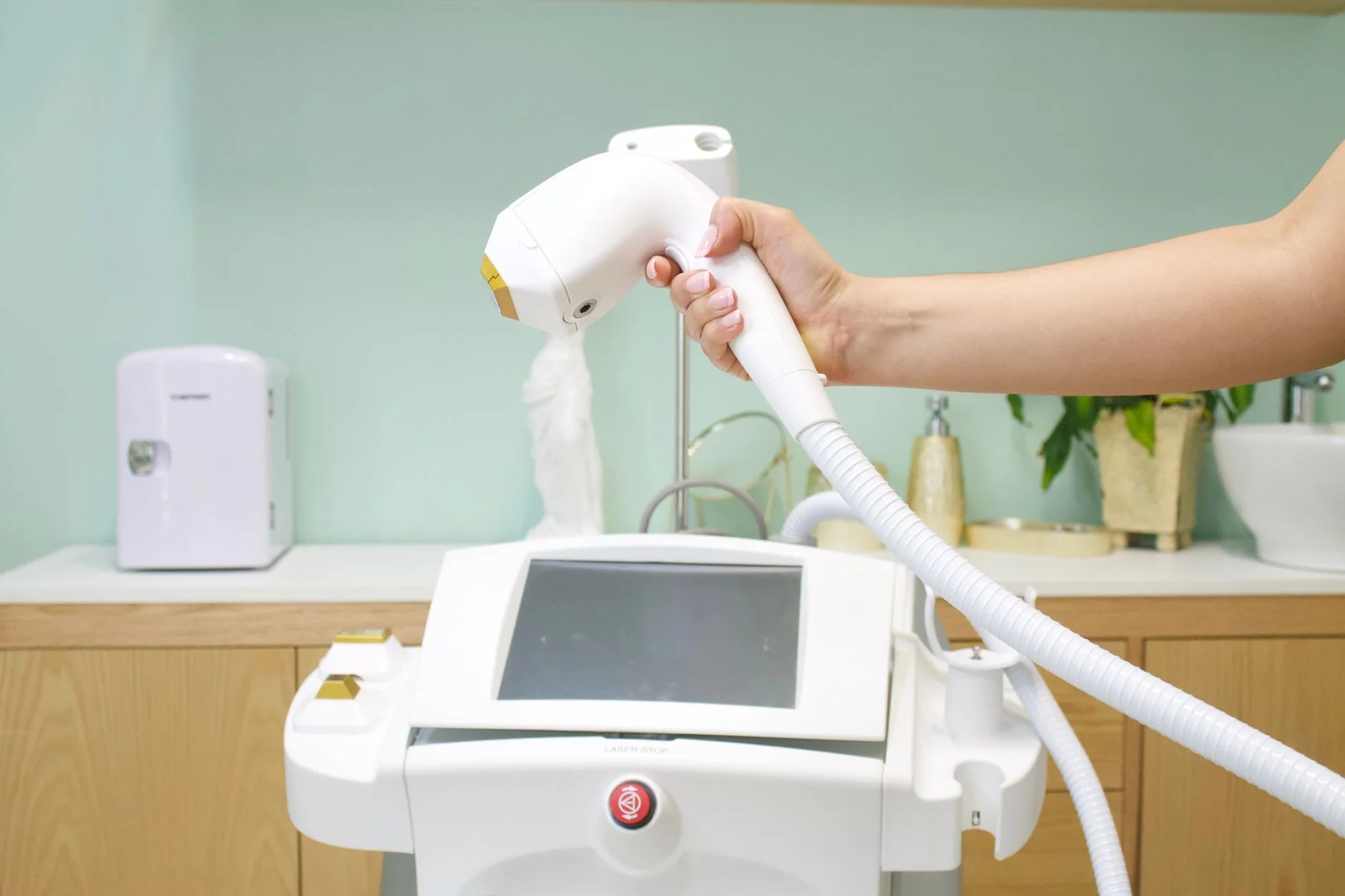 A practitioner holding a handheld hair removal device attached to a white treatment unit in a clinic room