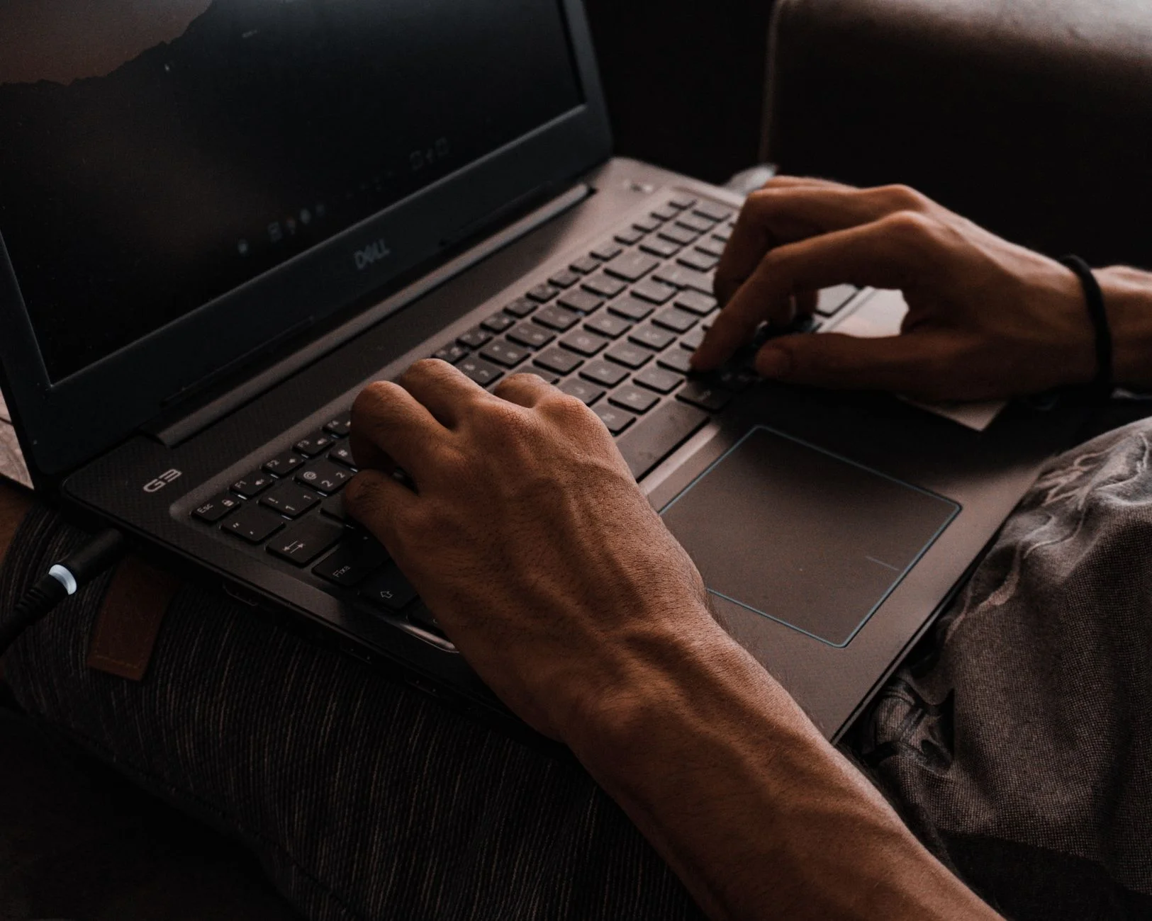 Close-up of a person’s hands typing on a laptop keyboard in a dark room