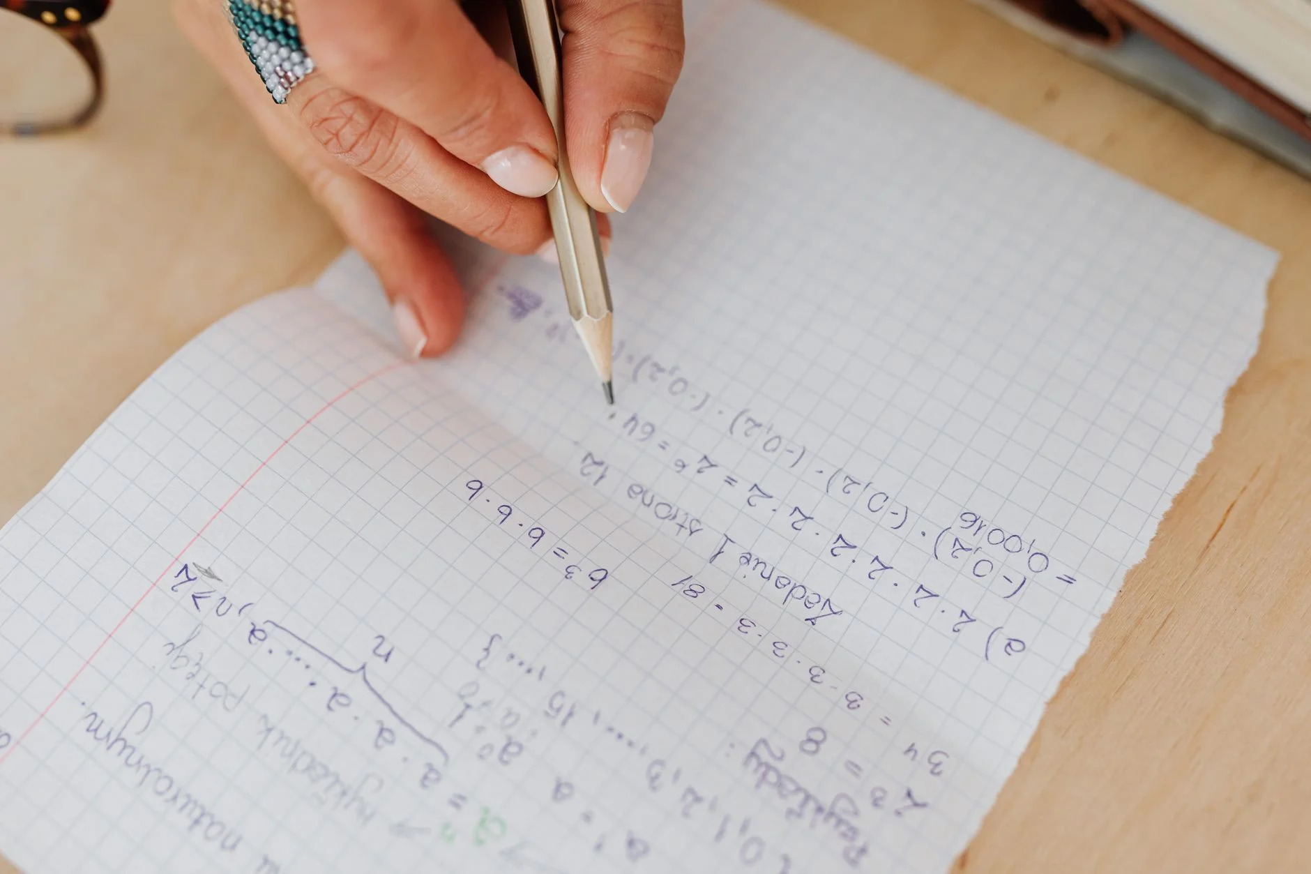 A hand writing equations in pencil on squared paper