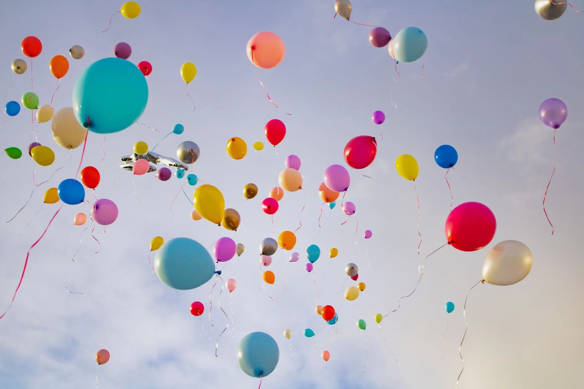 Many colourful balloons floating up into a pale sky