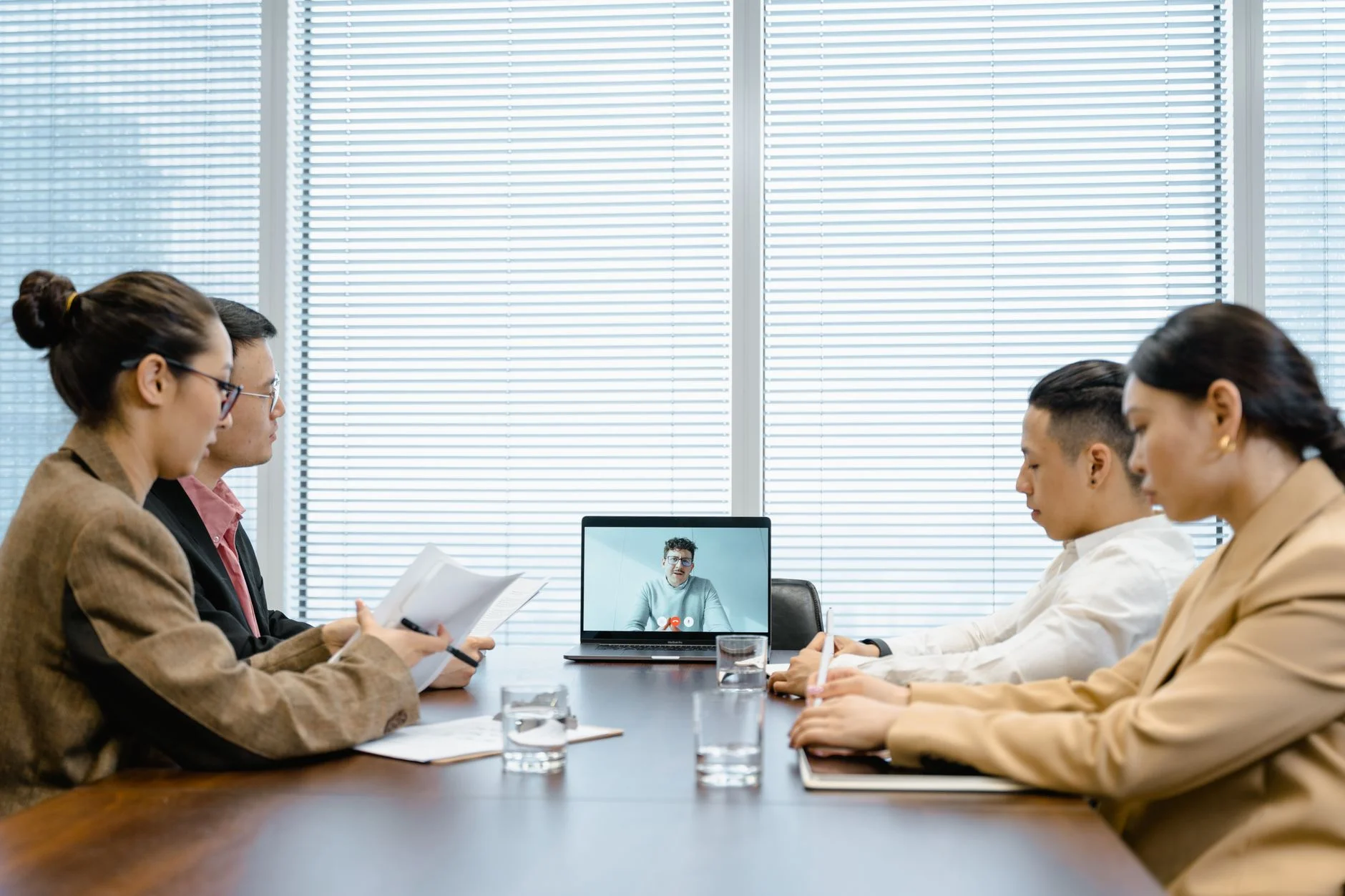 Four colleagues at a meeting table with a remote colleague on a laptop video call