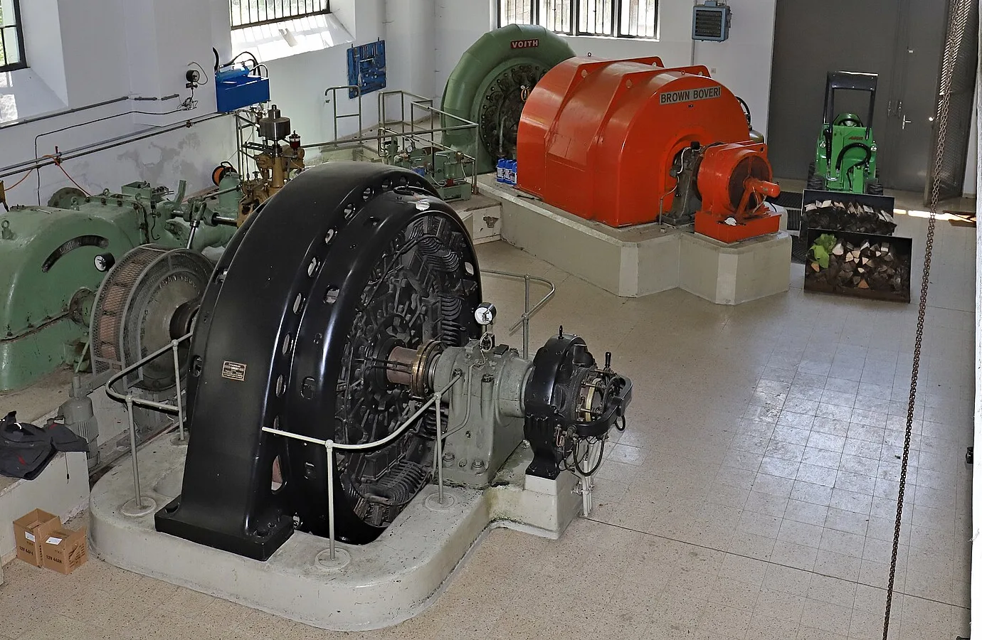 Large black, green and orange generators in the white engine hall of a small hydroelectric power plant