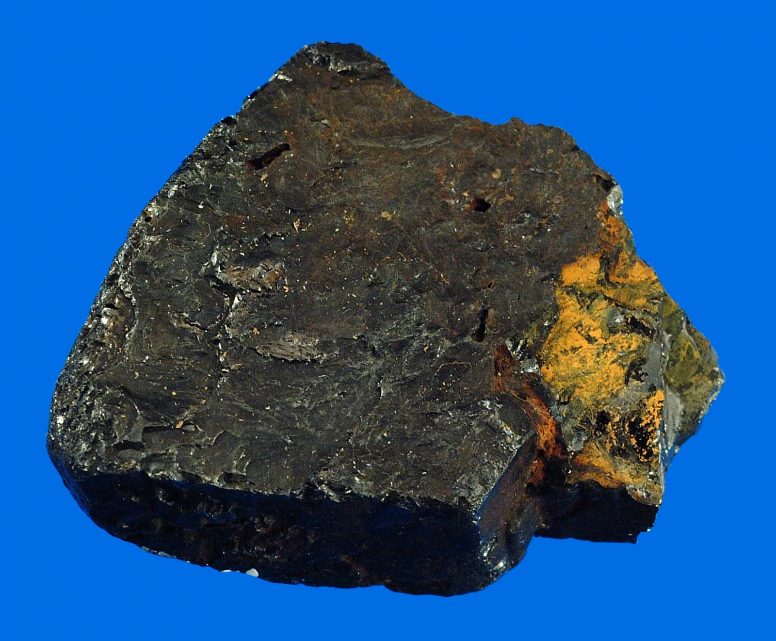 A dark, heavy lump of ilmenite, an iron titanium oxide ore, on a blue background