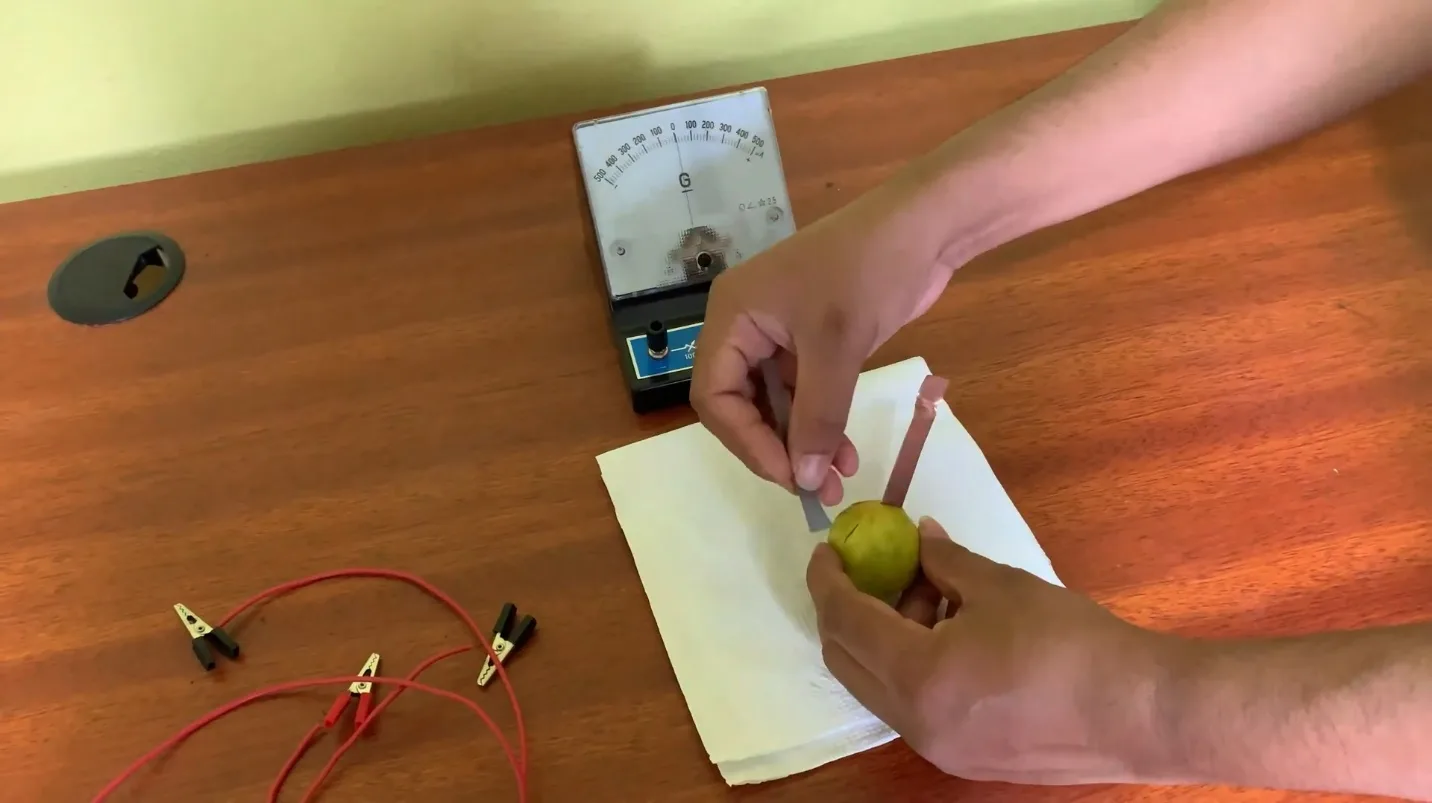 Hands pushing a zinc strip into a lime that already has a copper strip in it, on a paper towel