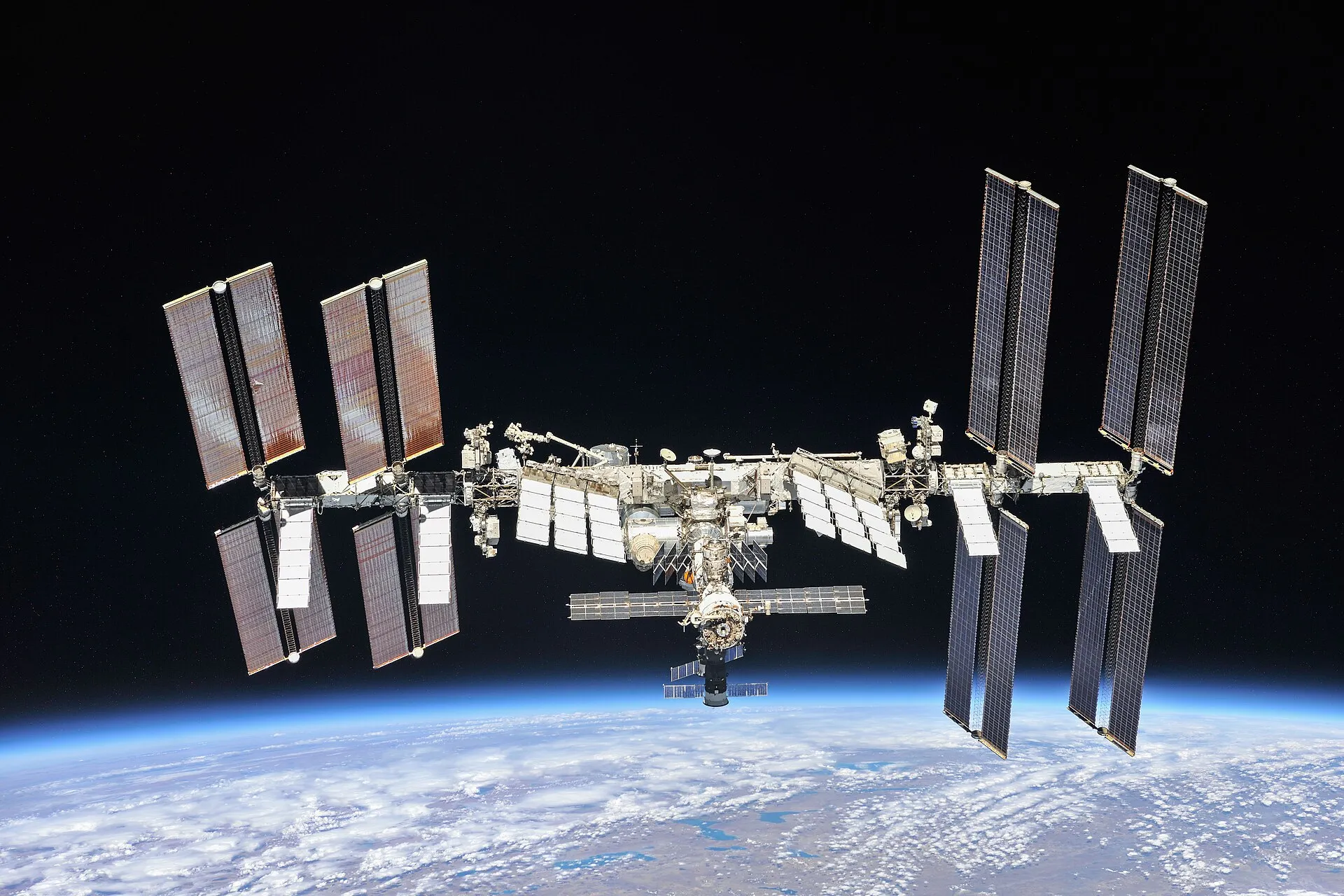 The International Space Station above Earth, with its long dark solar array wings spread out on both sides
