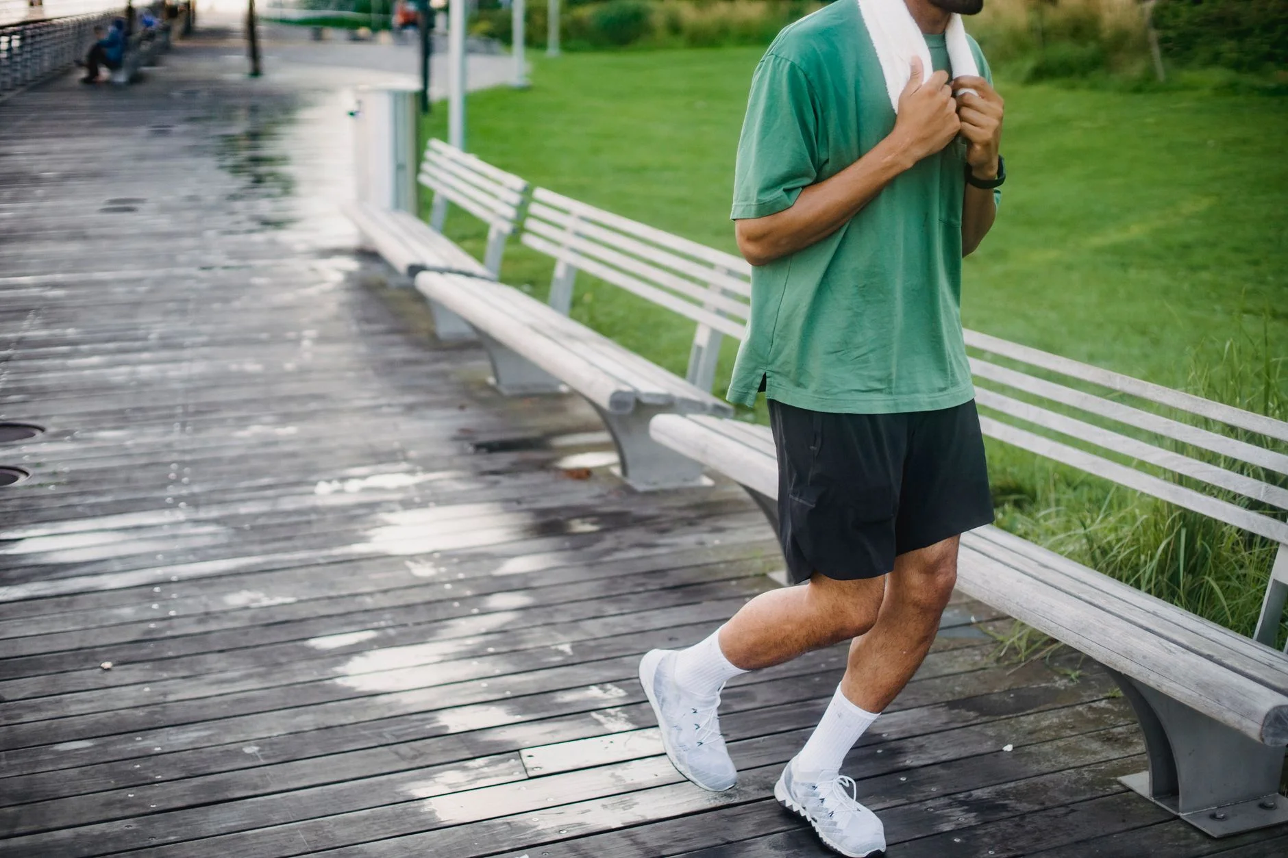 A man in a green T-shirt walking briskly along a wooden boardwalk in a park