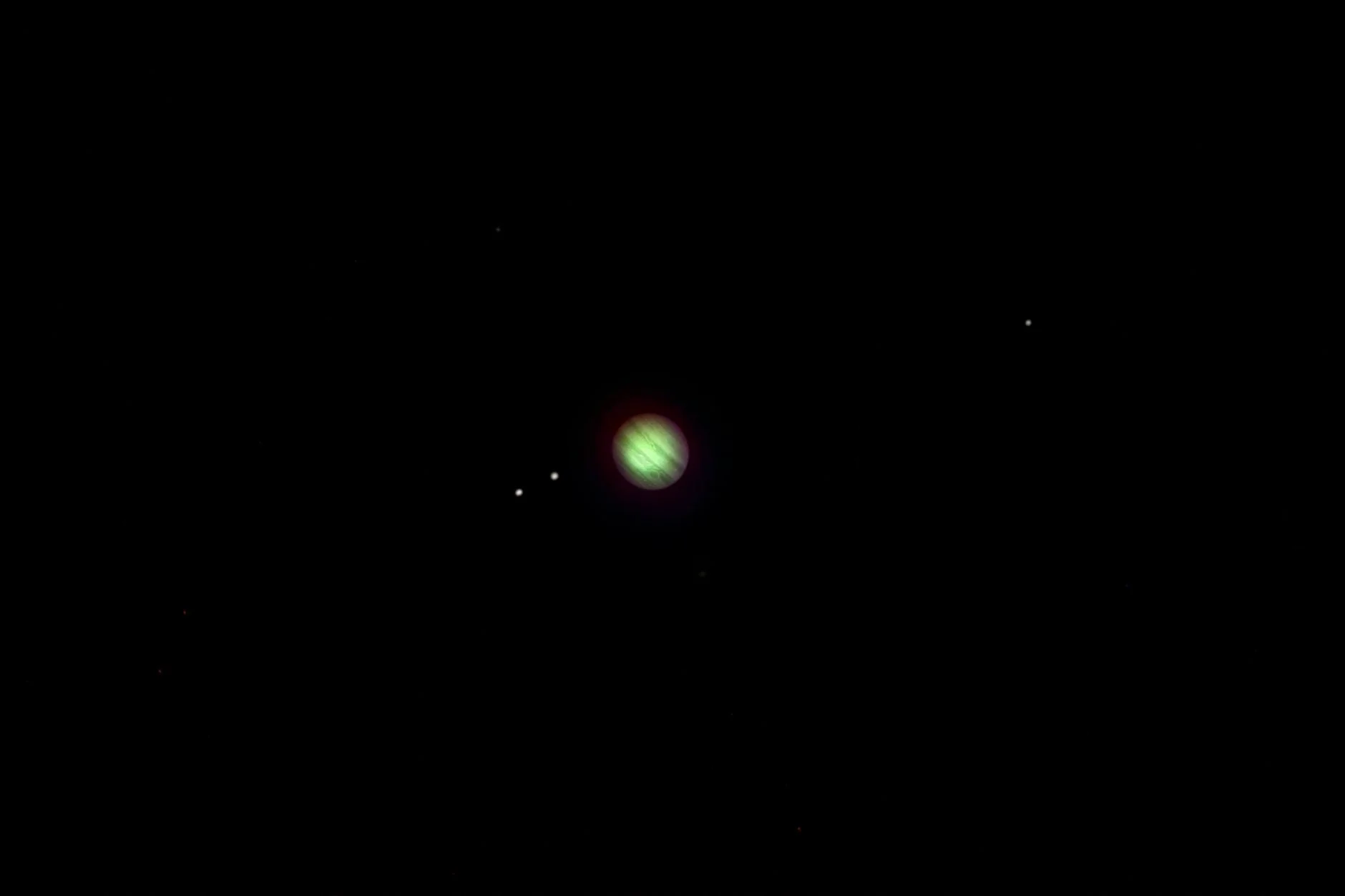 Jupiter, shown in processed colour, as a small disc with three of its moons nearby
