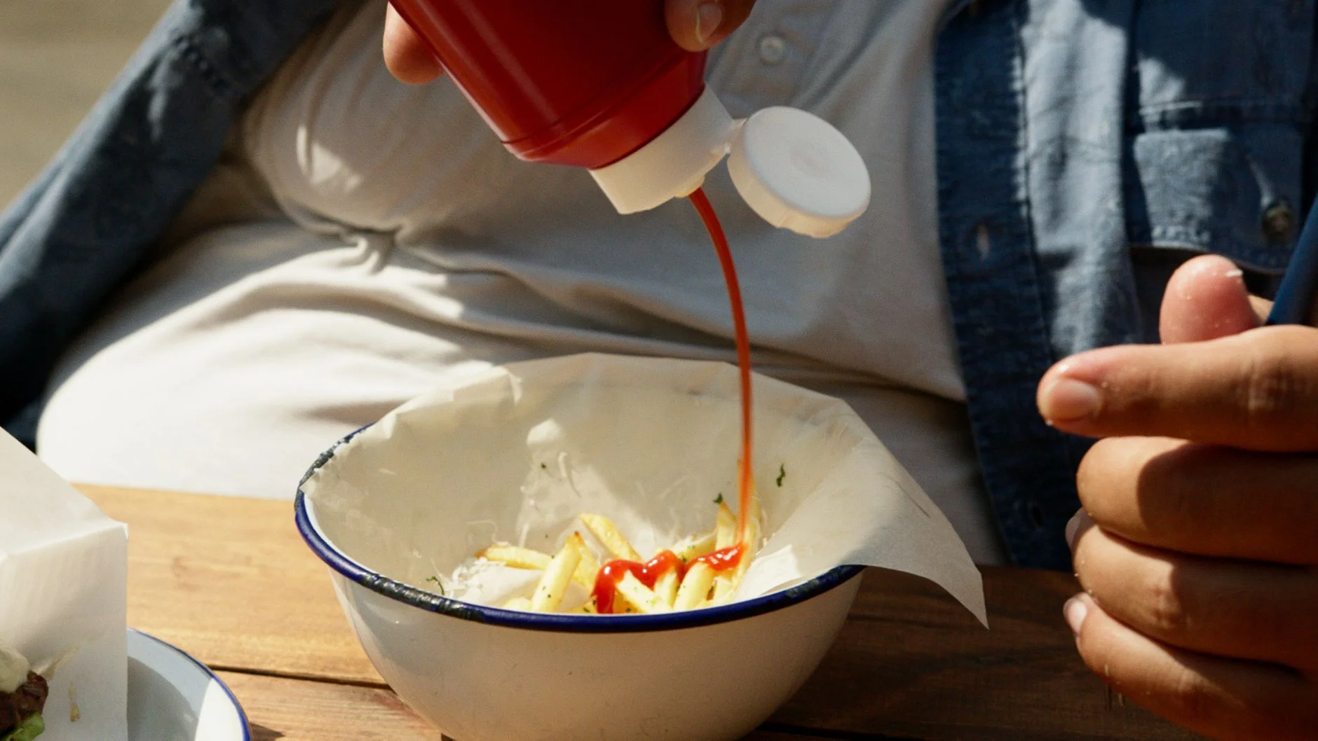 Ketchup being squeezed from a red bottle onto chips in a bowl