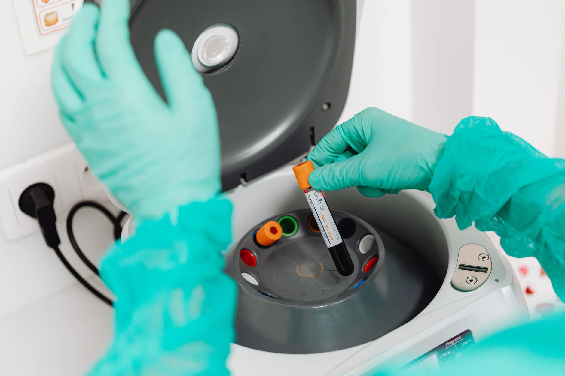 A gloved laboratory worker placing a blood sample tube into a centrifuge